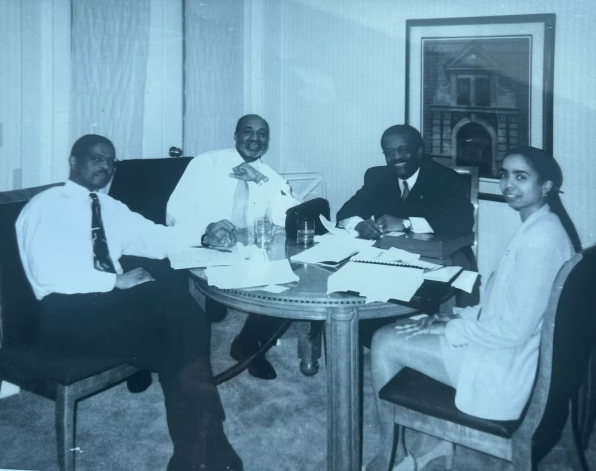 Four people seated around a small table in an office, appearing to discuss documents.
