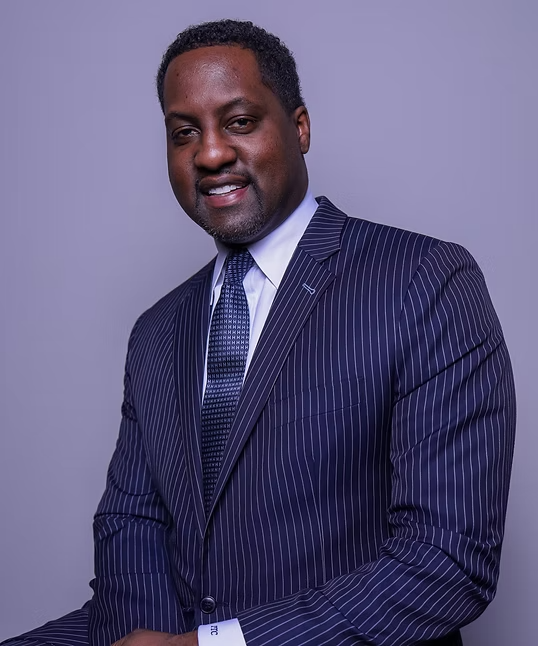 Man in a navy pinstripe suit smiling against a light purple studio background