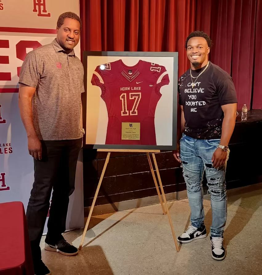 Two men posing beside a framed red football jersey on an easel at an event