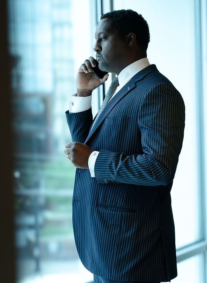 Man in a blue pinstripe suit talking on a phone by a bright office window