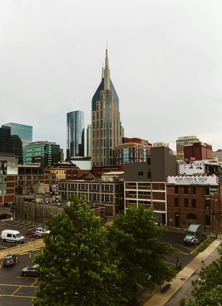 City skyline with a tall Art Deco tower above low-rise buildings and trees under an overcast sky