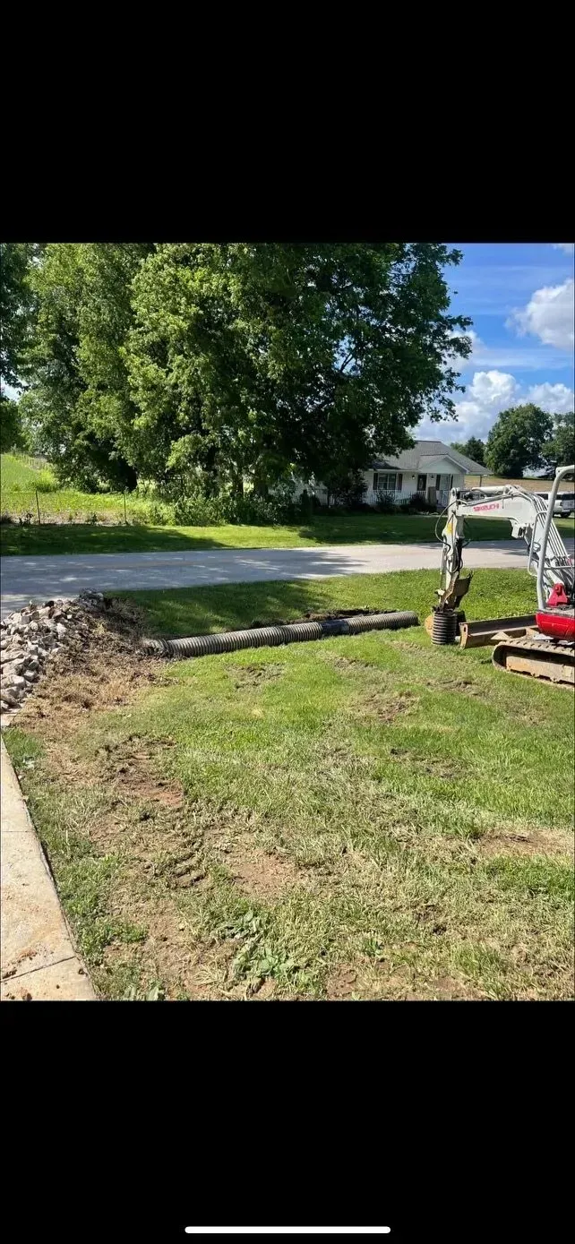 A red excavator is digging a hole in the grass in front of a house.