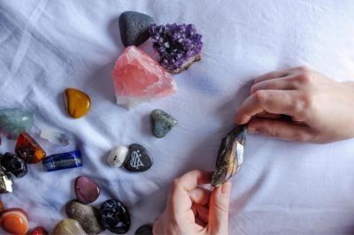 Hands holding a polished crystal over assorted colorful crystals on a white cloth