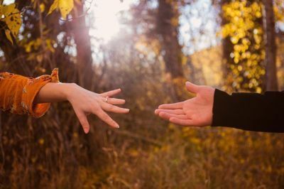 Two hands reaching toward each other in a sunlit autumn forest