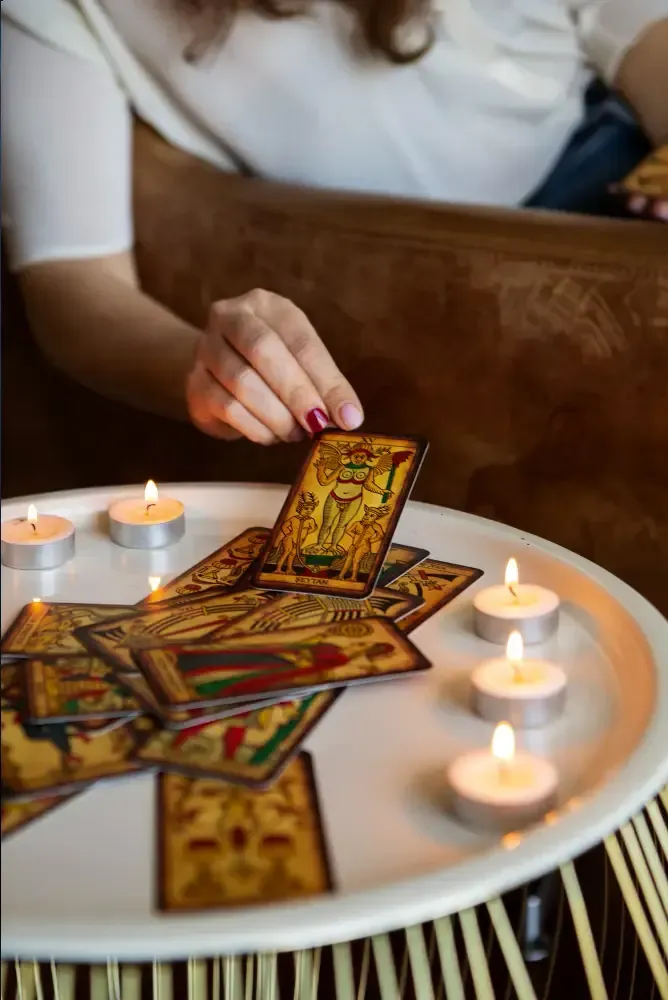 Hand placing tarot cards on a lit candlelit table