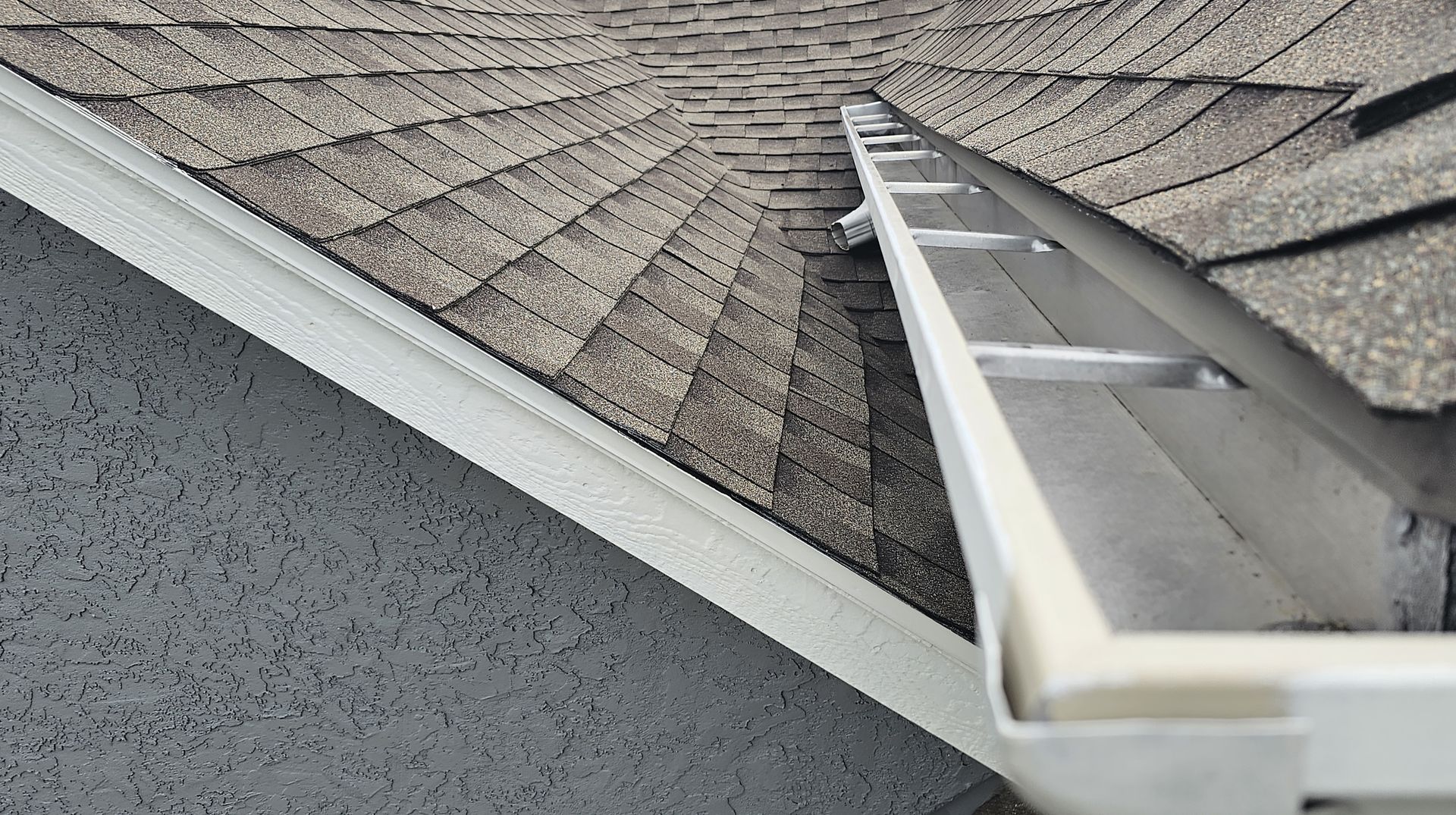 A gutter on the side of a house next to a roof.