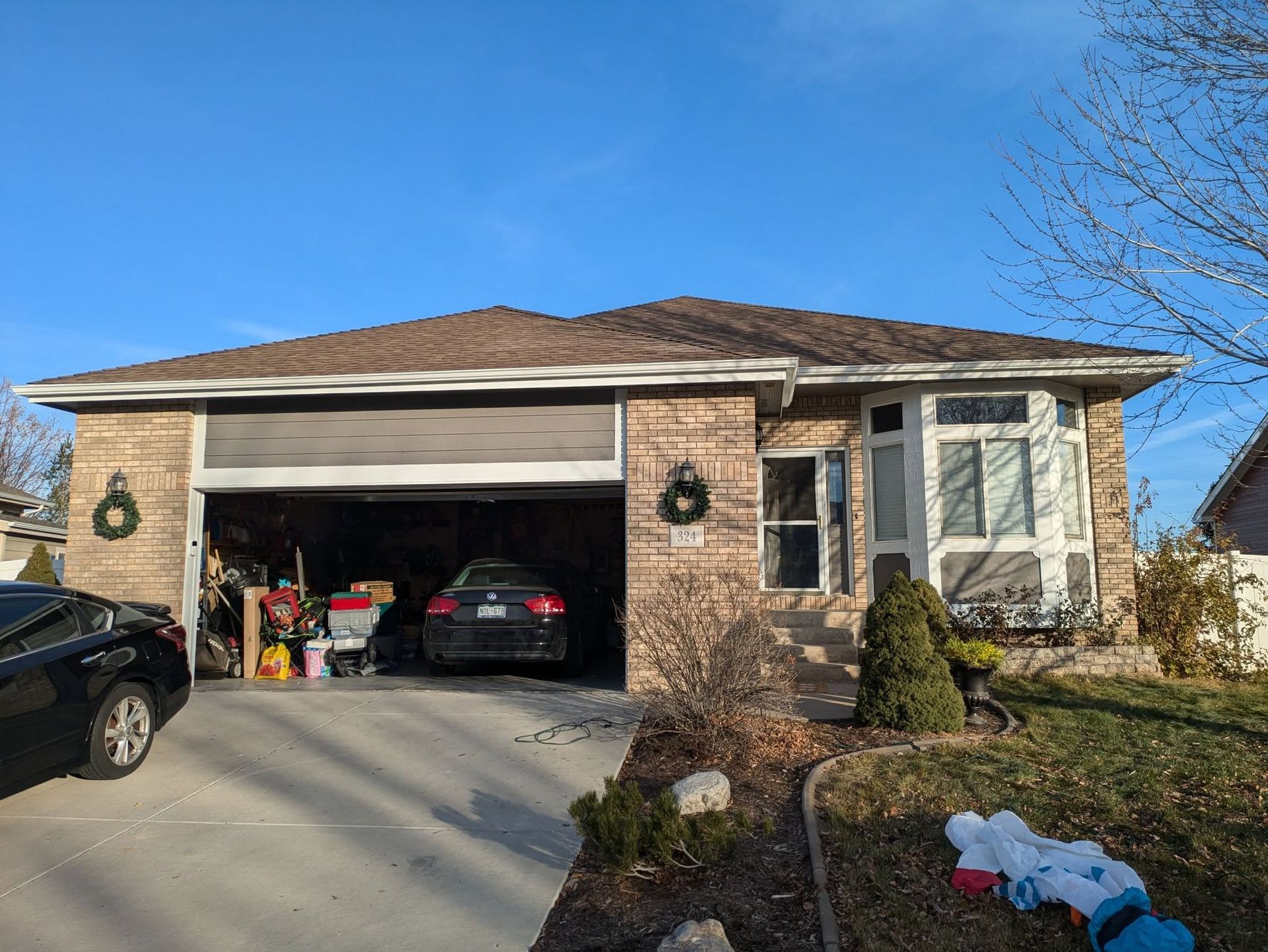 Single-story brick house with open garage, cars in driveway, and a snowy front yard.