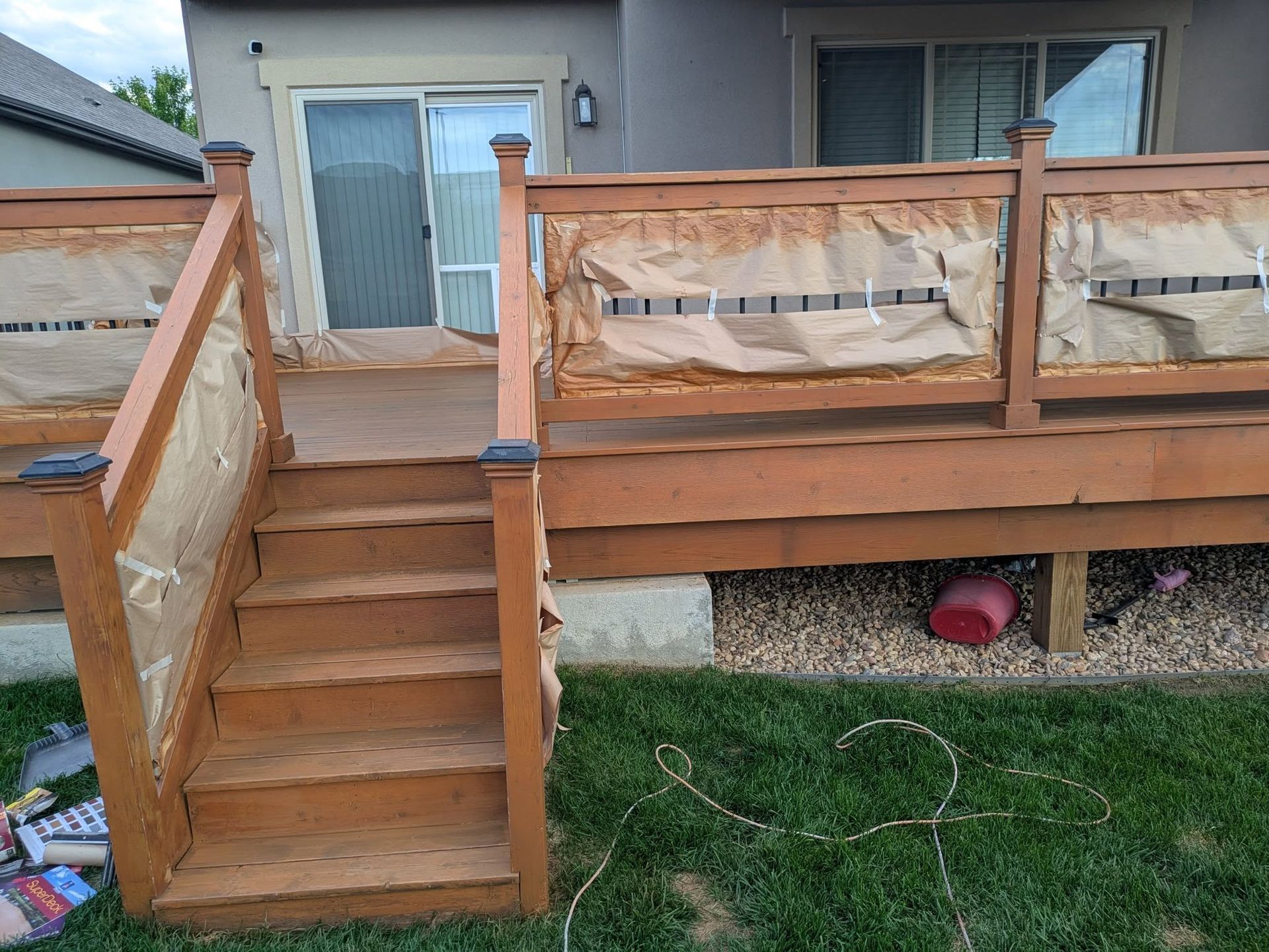 Wooden backyard deck with stairs leading to a house’s sliding glass door and window.