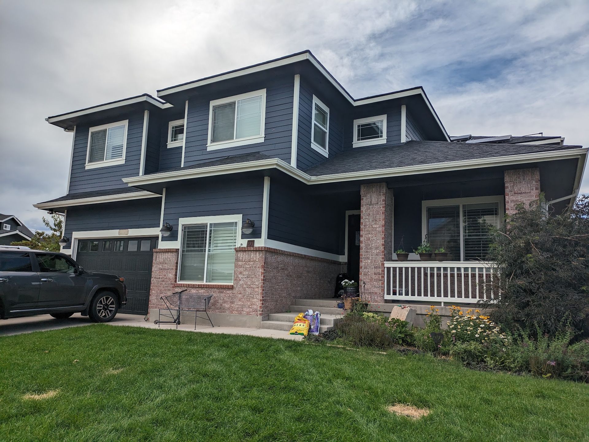 Two-story blue house with brick trim, front porch, and a parked car beside a green lawn.