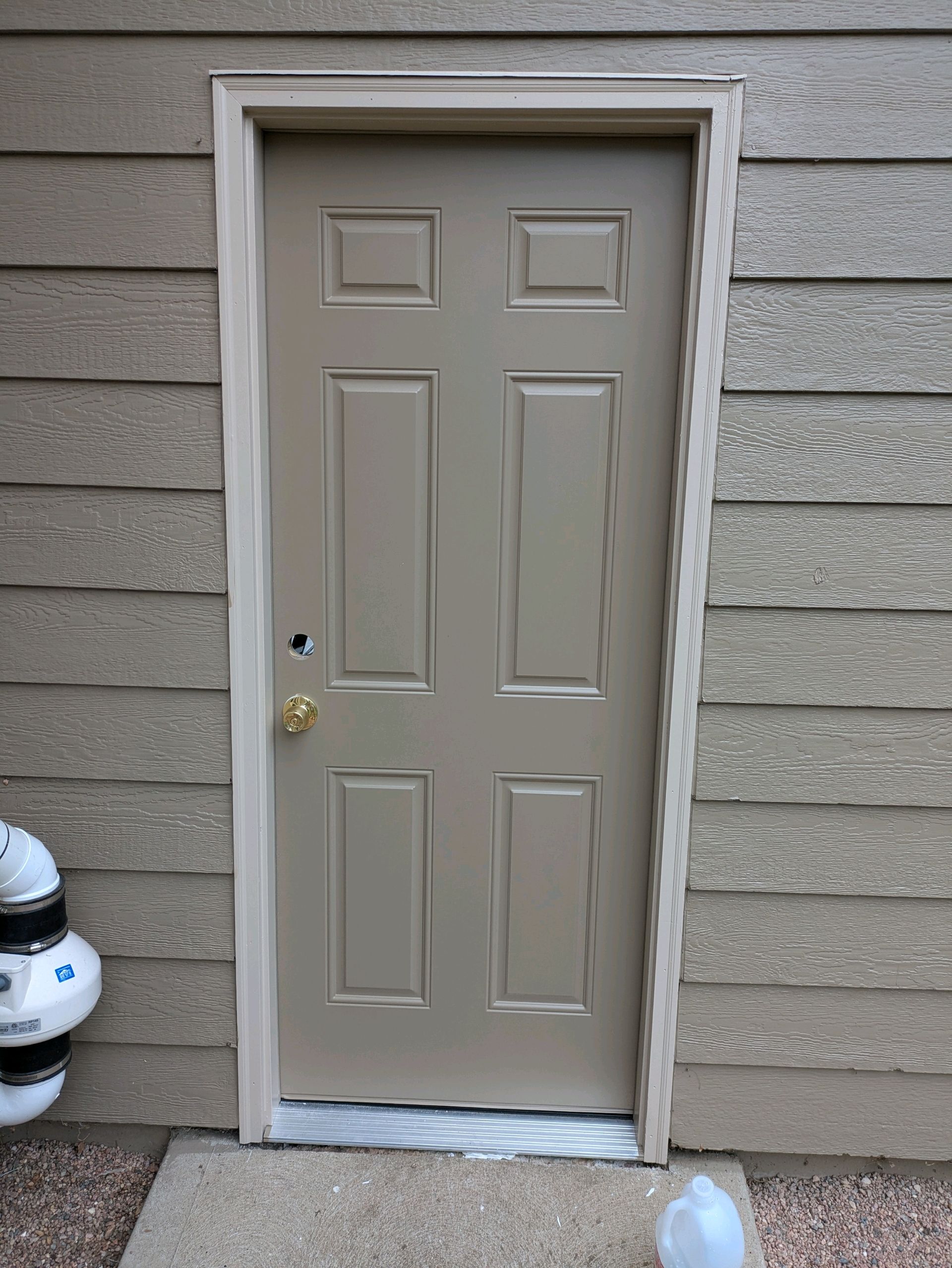 Beige exterior door in tan siding wall, with a brass handle and snow at the threshold.