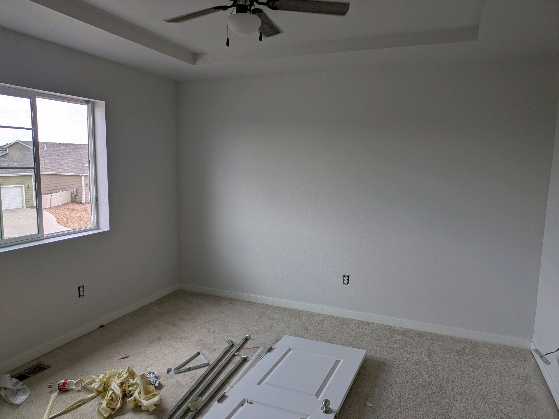 Empty bedroom with gray walls, a window, ceiling fan, and construction materials on the floor