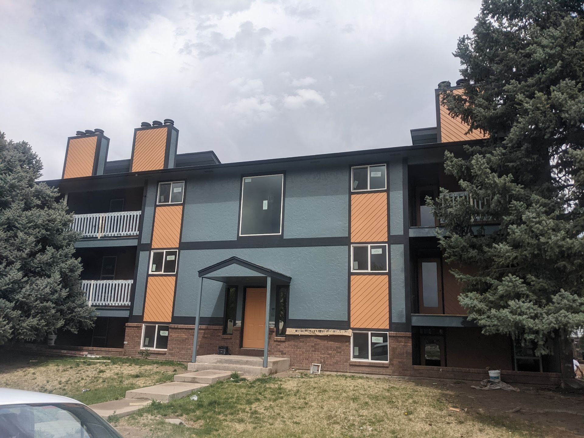 Apartment building exterior with teal siding, orange accents, and balconies under a cloudy sky