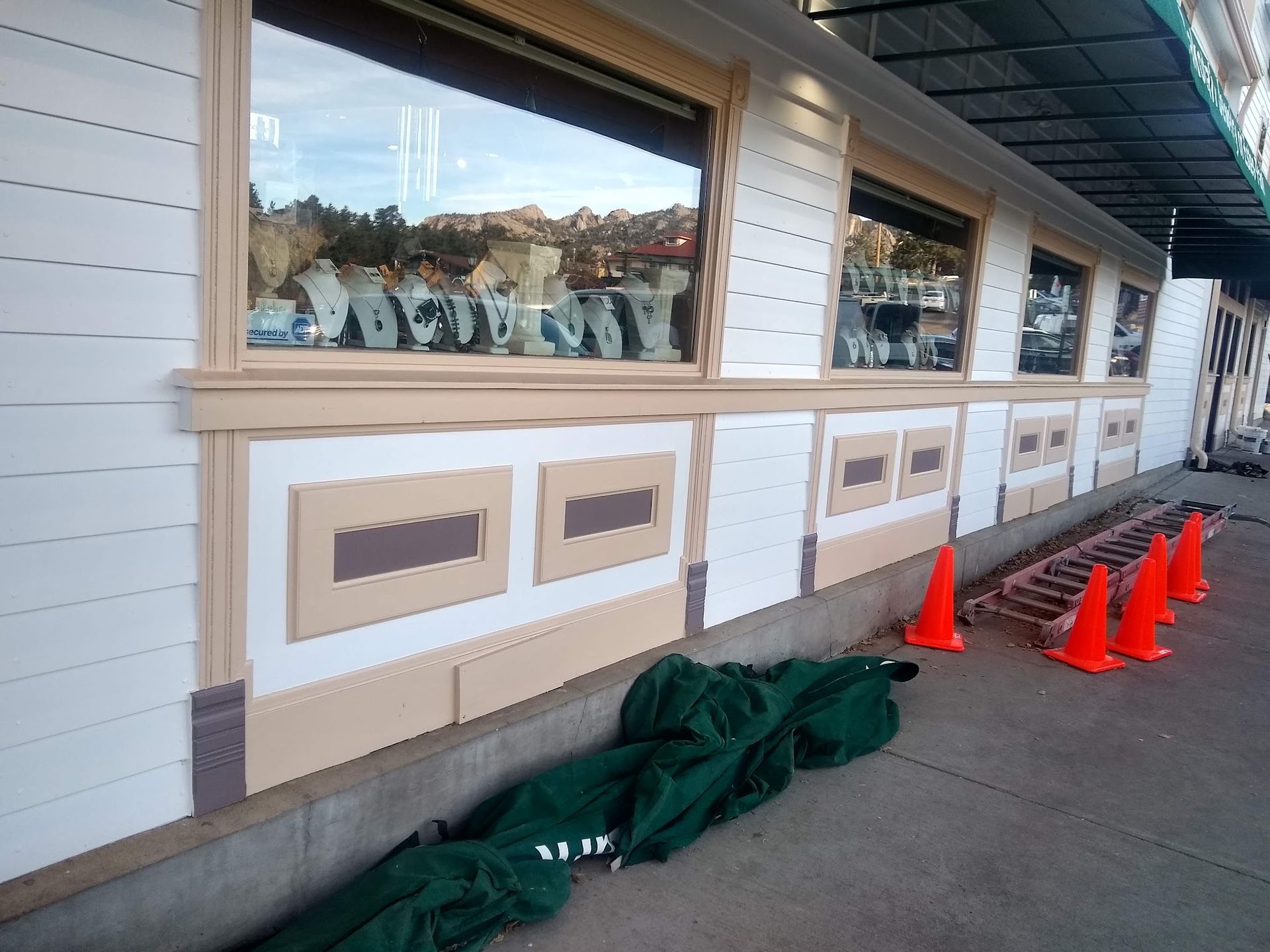 Storefront wall with covered windows, orange cones, and green tarps along a sidewalk