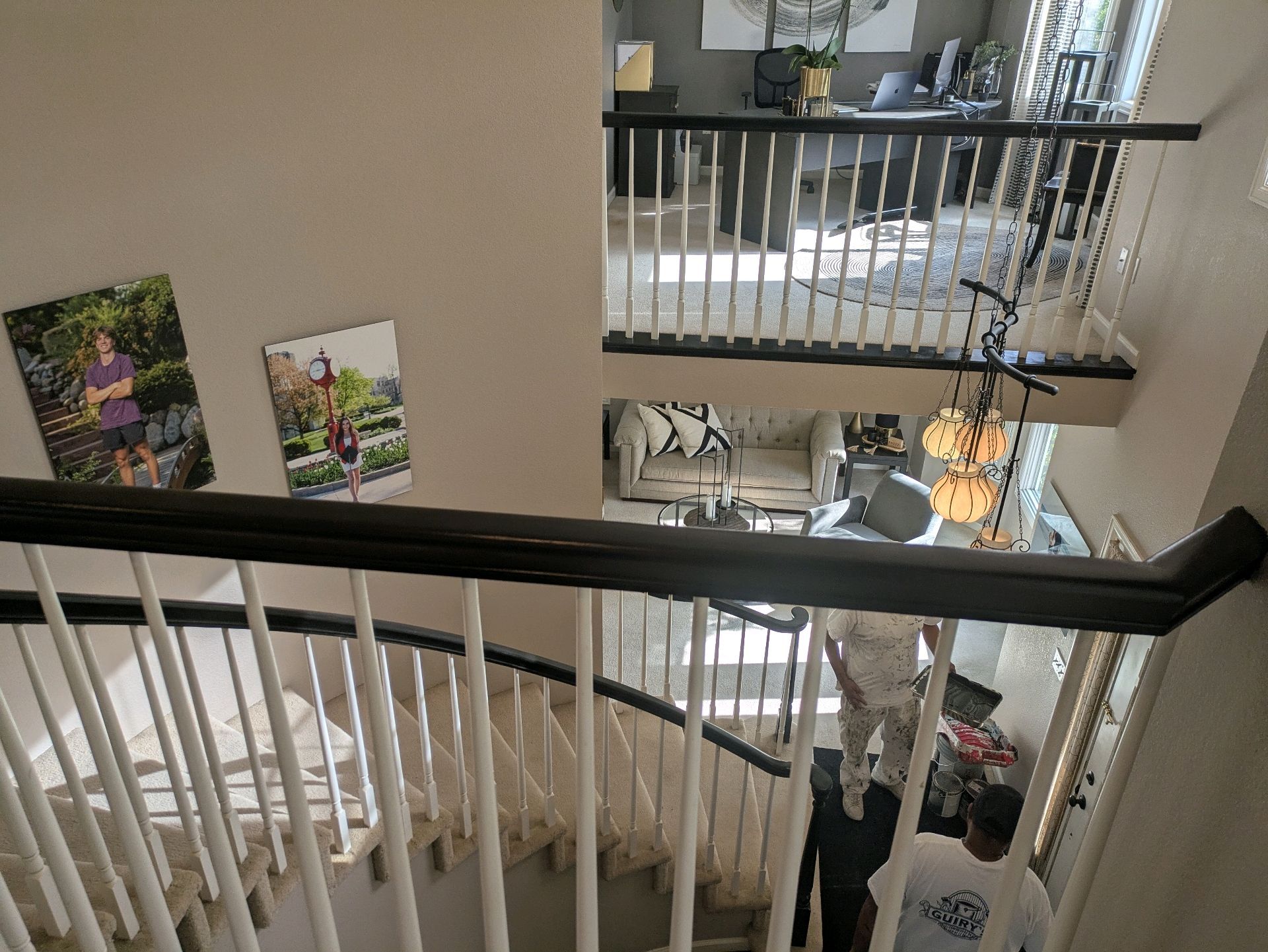 Indoor stairwell with black railings, wall art, and bright living area below.