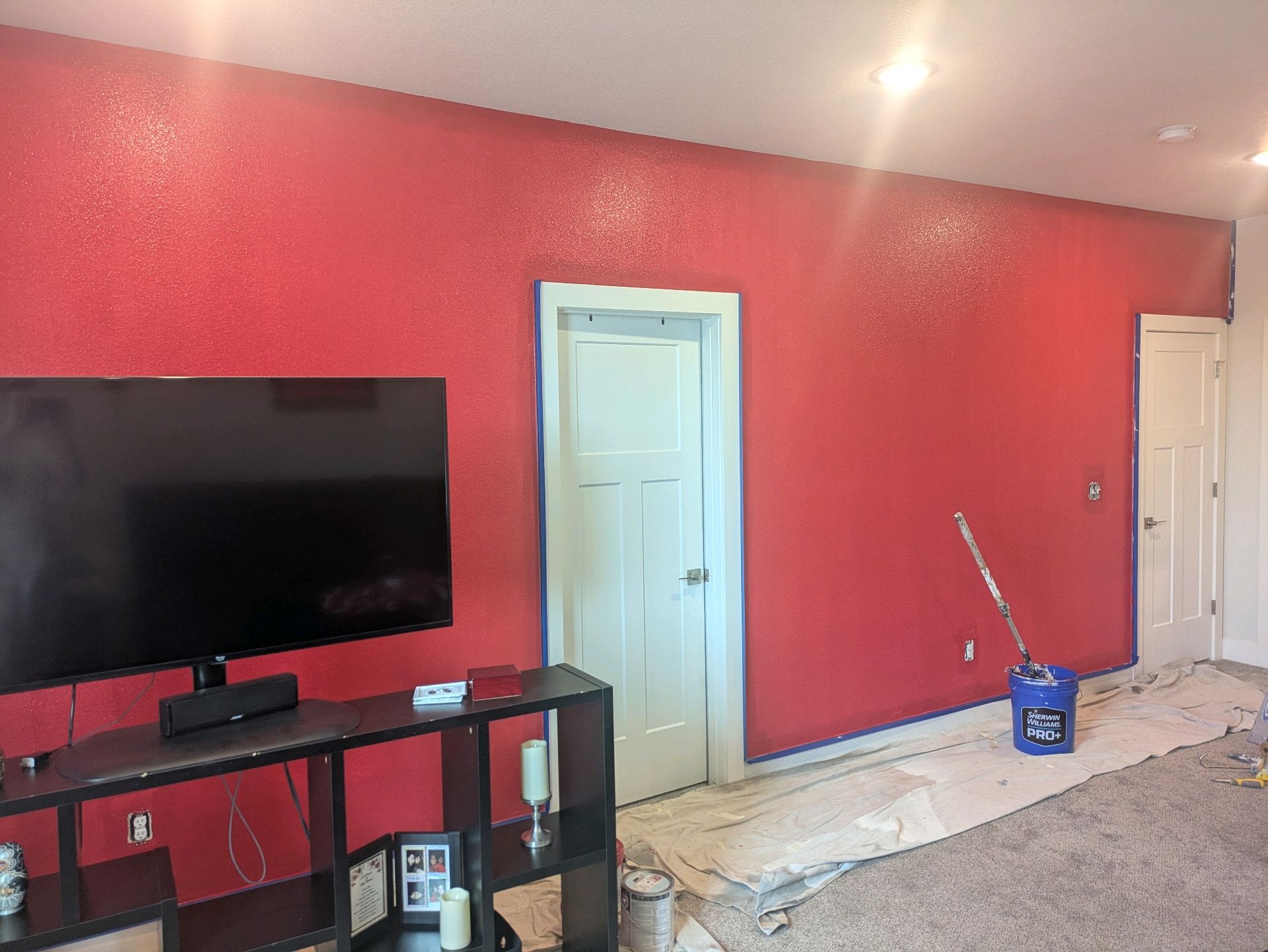 Room with red walls, a wall-mounted TV, and a door under renovation with tools and materials on the floor