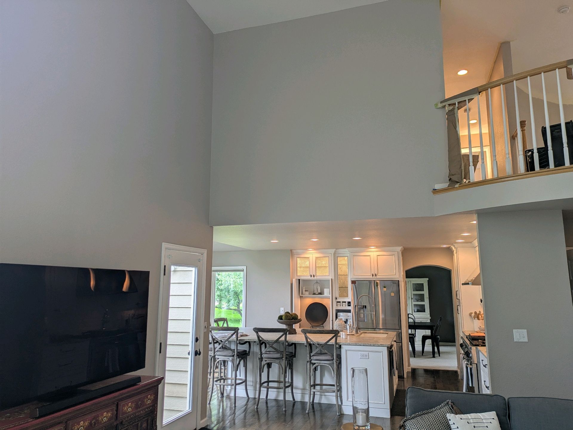 Open living room with tall ceiling, large TV, and kitchen/dining area beyond the open space