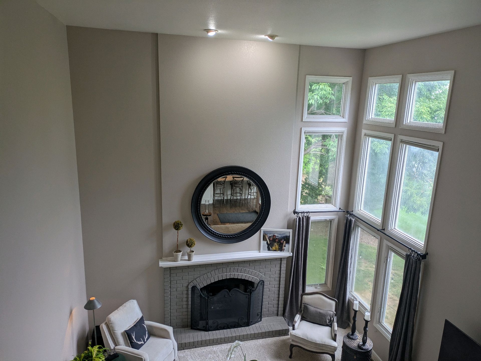 Living room with fireplace, round mirror, beige walls, and tall windows with sheer curtains