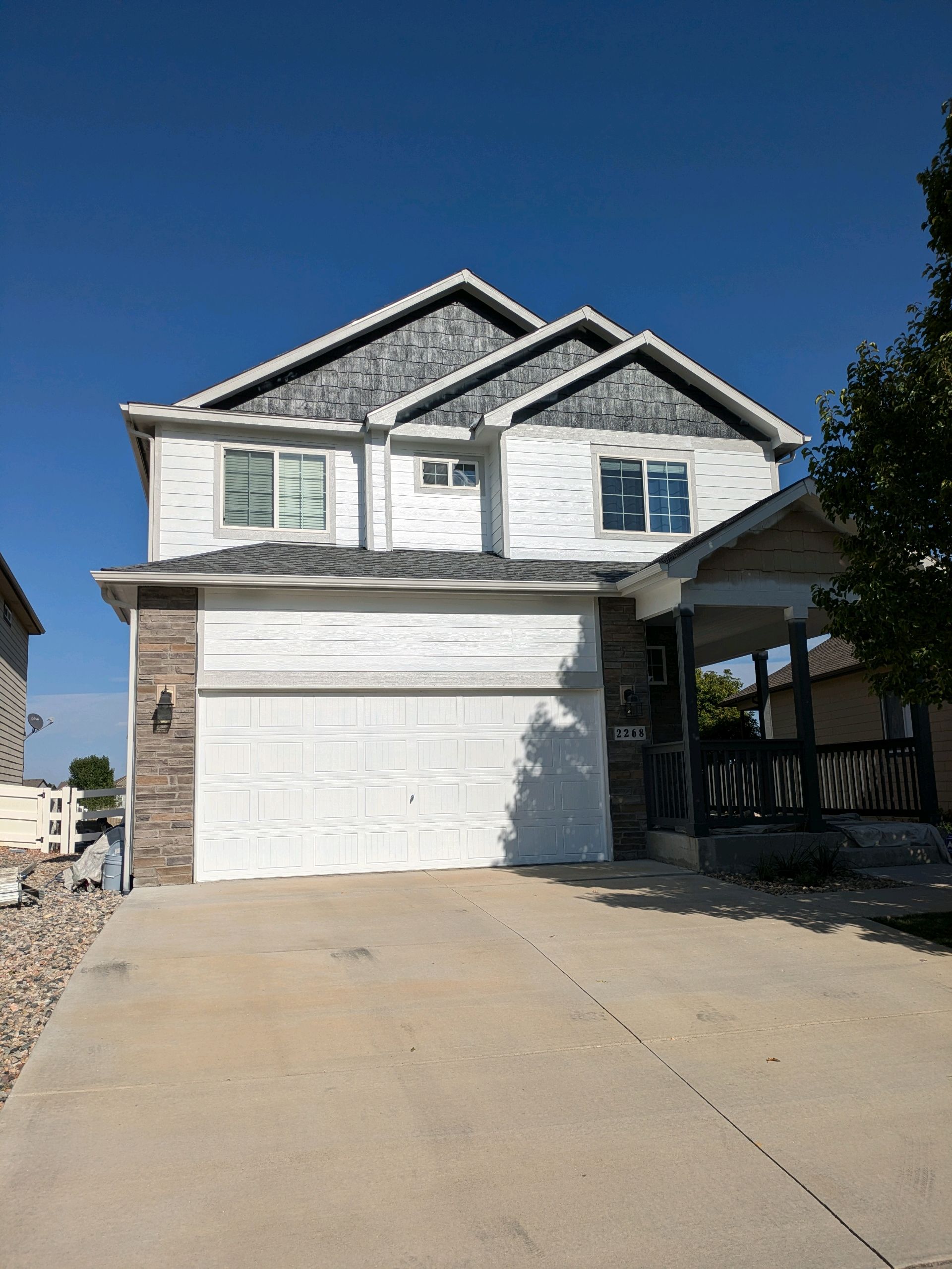 Two-story white house with a double garage and concrete driveway under a clear blue sky