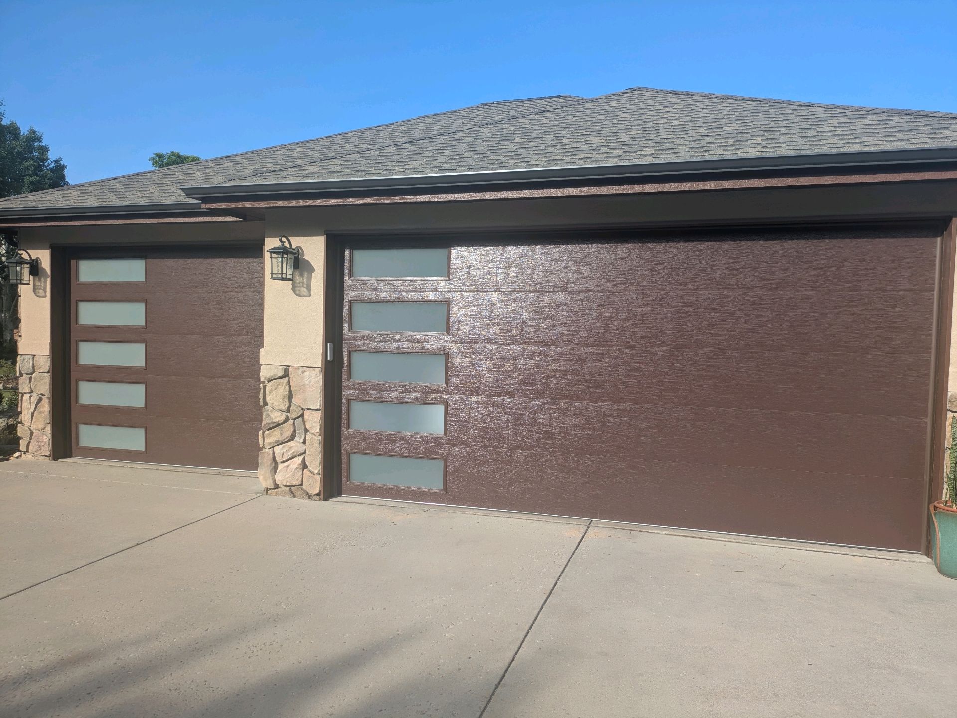 Two-car brown garage with frosted glass door panels and stone column by a concrete driveway