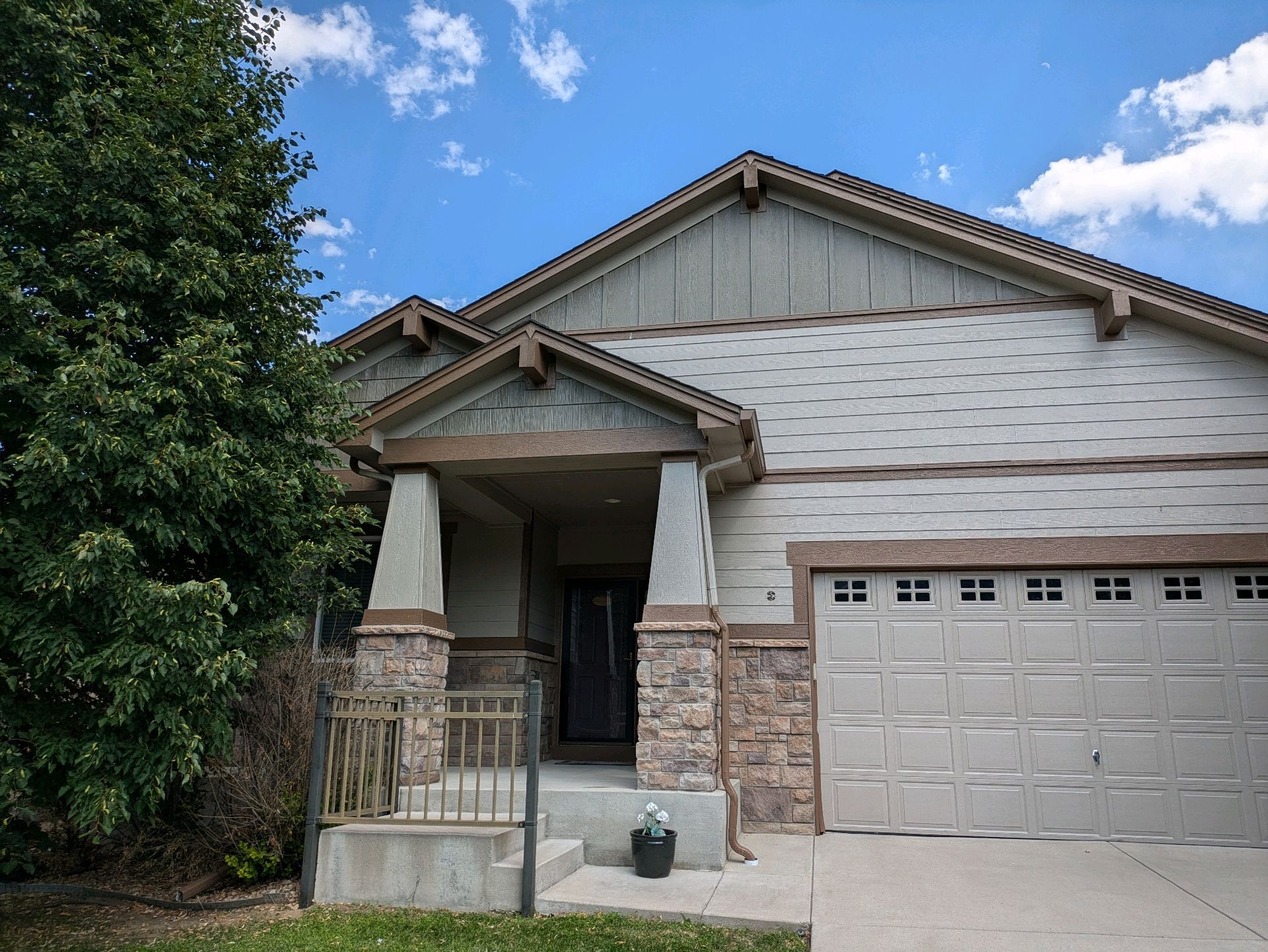 Suburban house with stone and beige siding, front porch, garage, and a blue sky with clouds