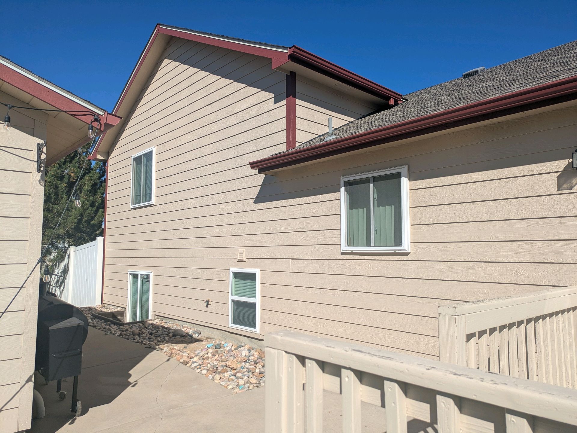 Beige house exterior with white-trimmed windows, red roof accents, and a side walkway under bright sun