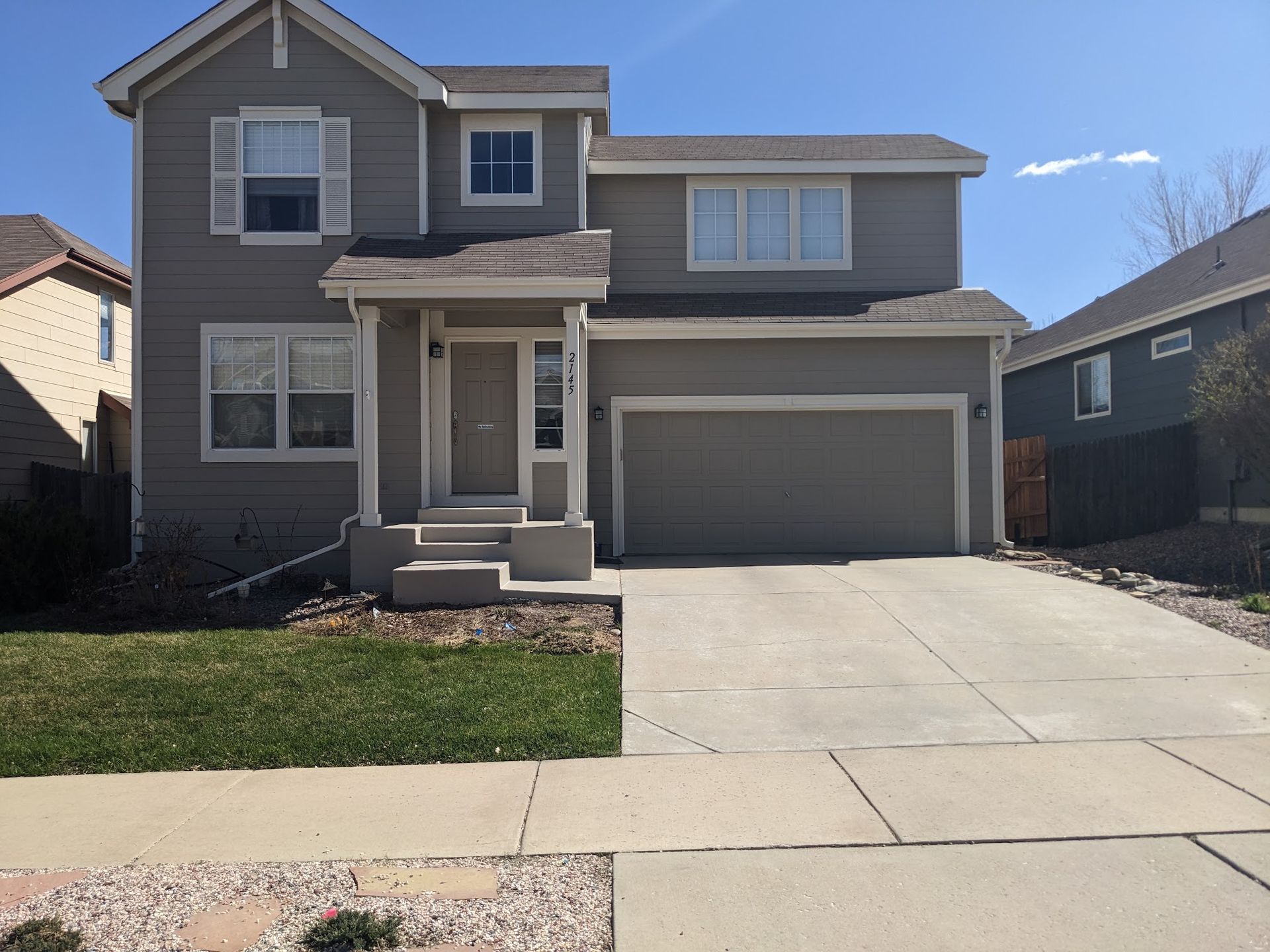 Two-story suburban house with a front porch, garage, and concrete driveway under a clear sky
