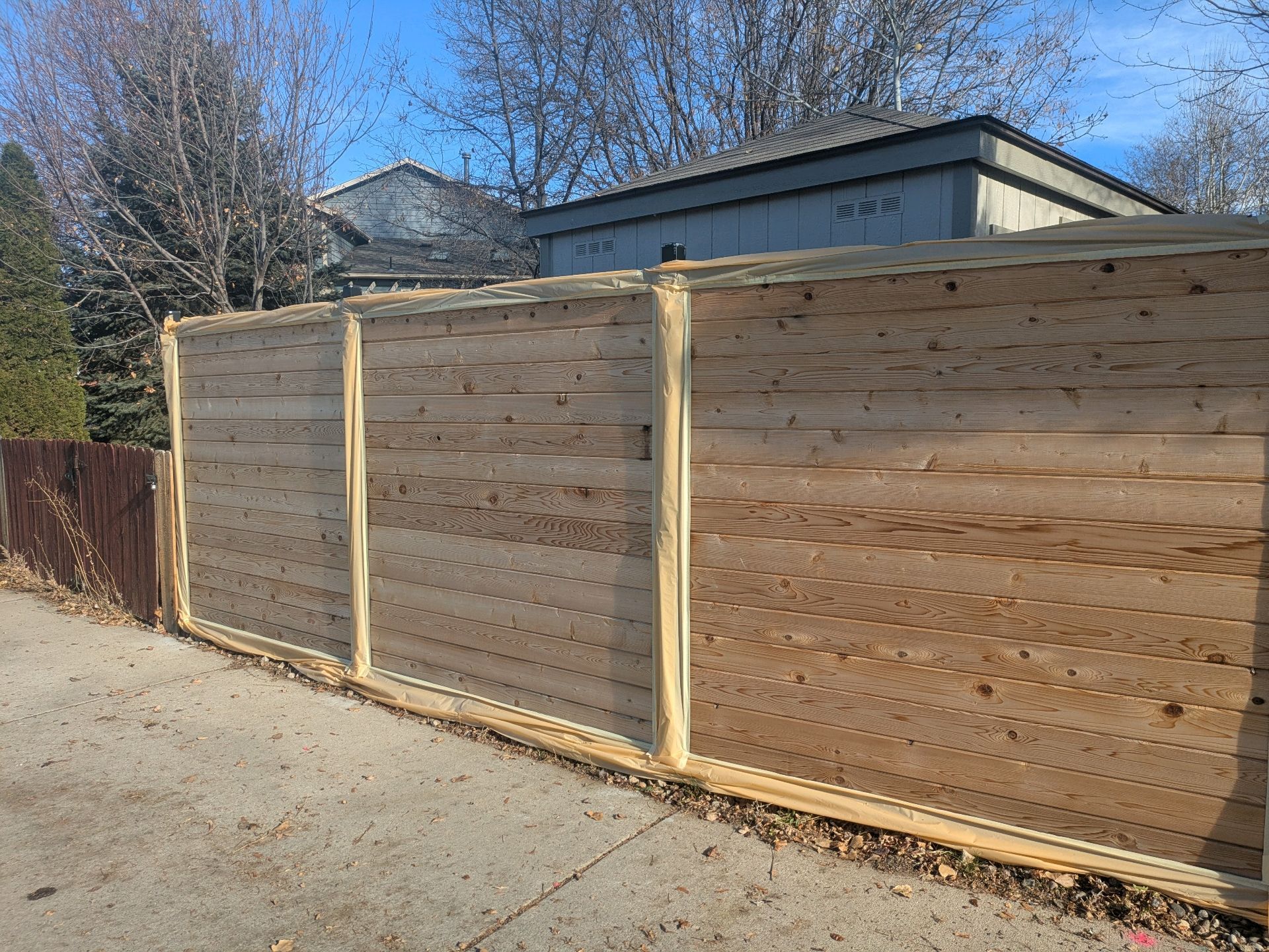 Wooden privacy fence along a gravel roadside under a blue sky
