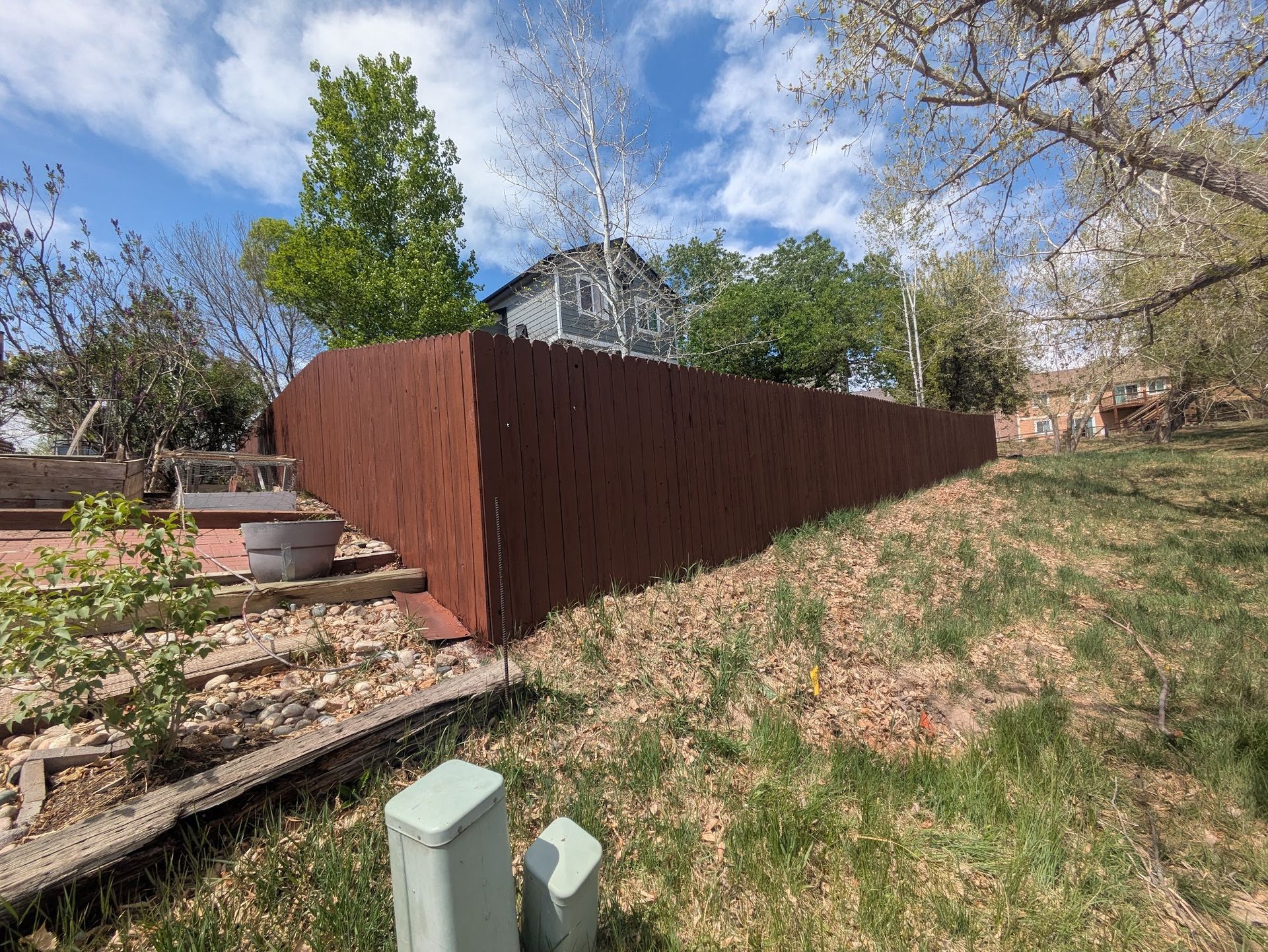 Rusty brown corrugated metal fence along a sloped grassy yard under a blue sky.