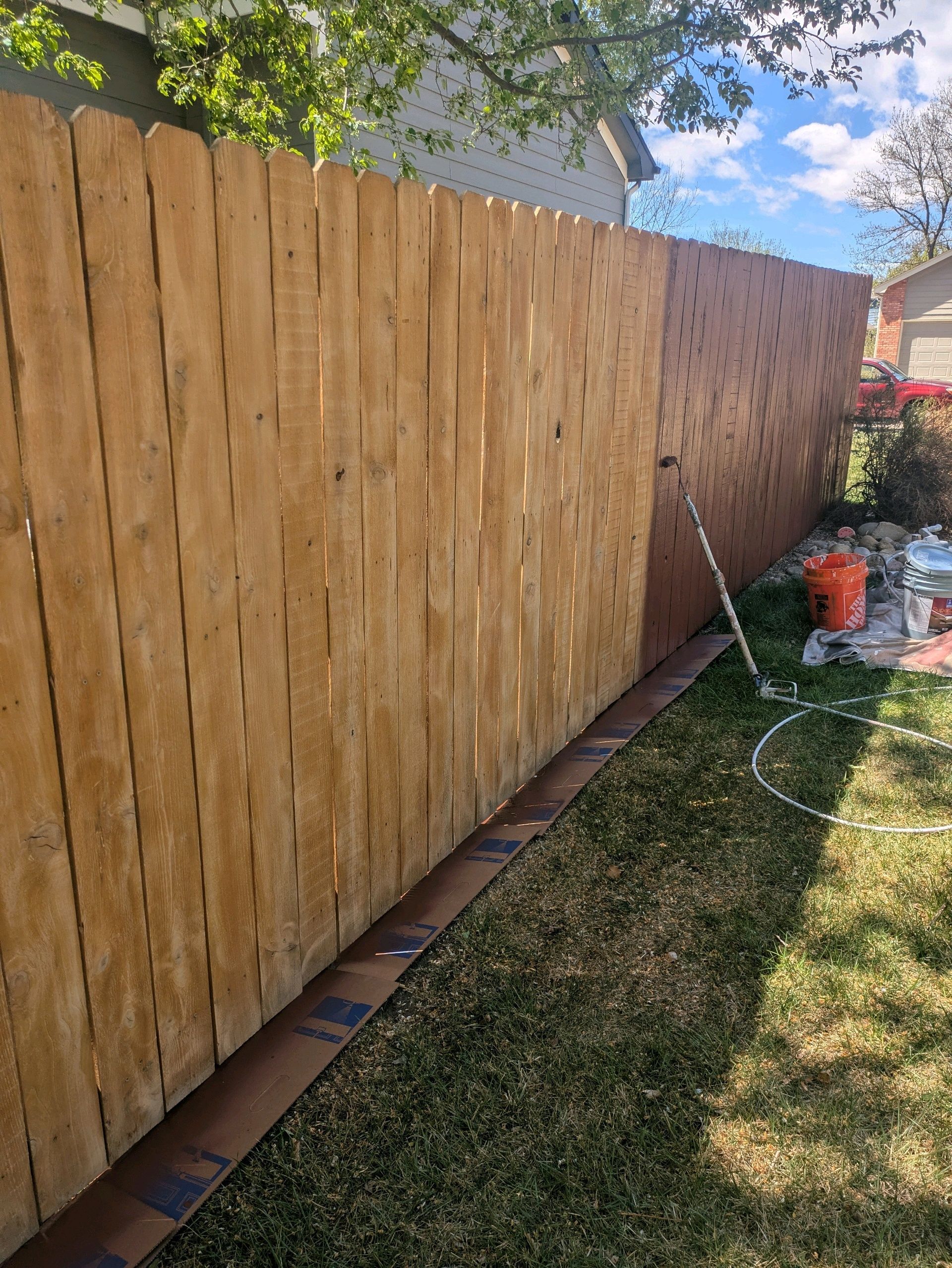 Wooden privacy fence along a grassy yard with a garden hose and potted plants on the right.