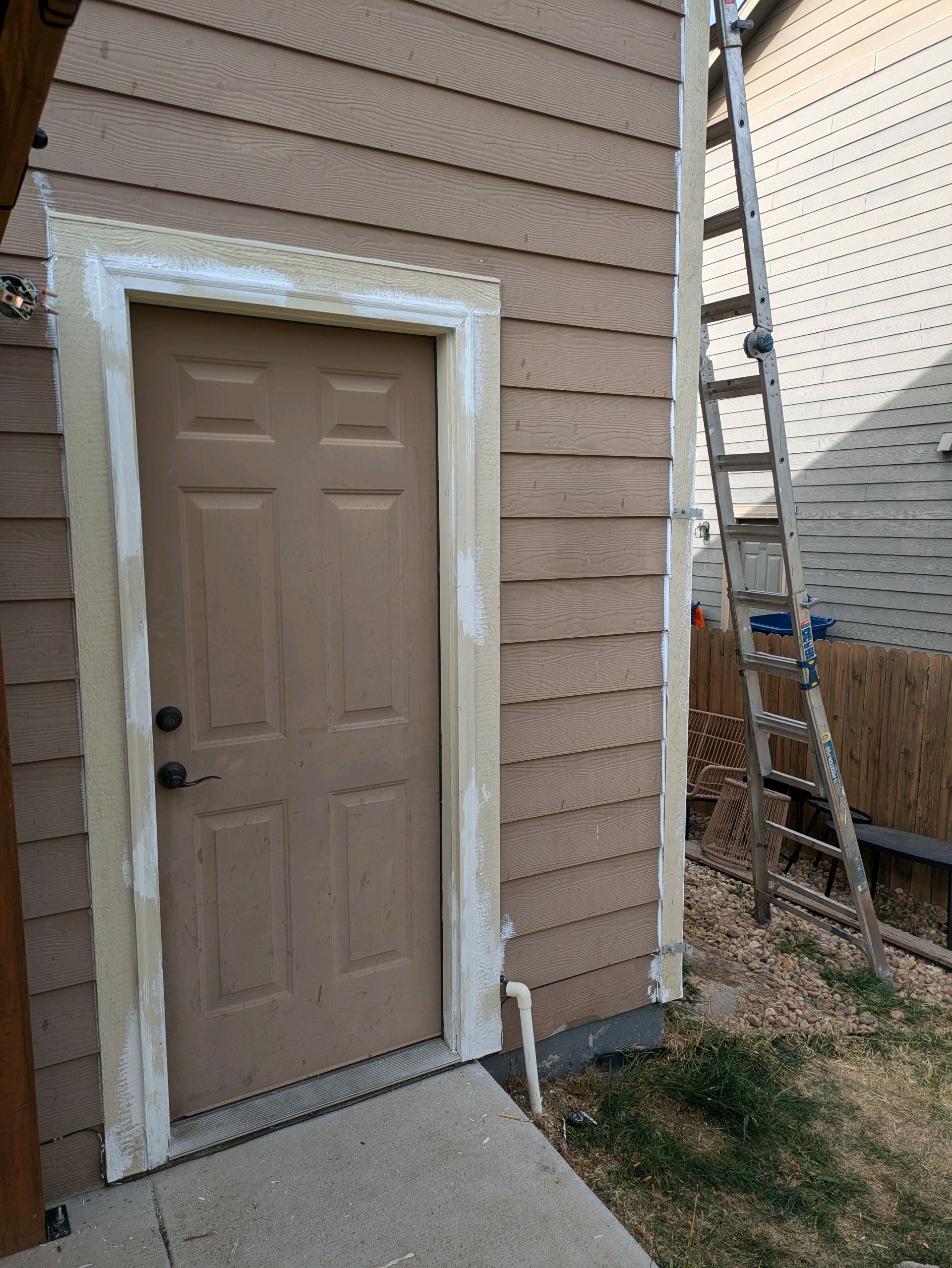 Beige side door with white trim on a townhouse exterior, beside a narrow walkway and fence.
