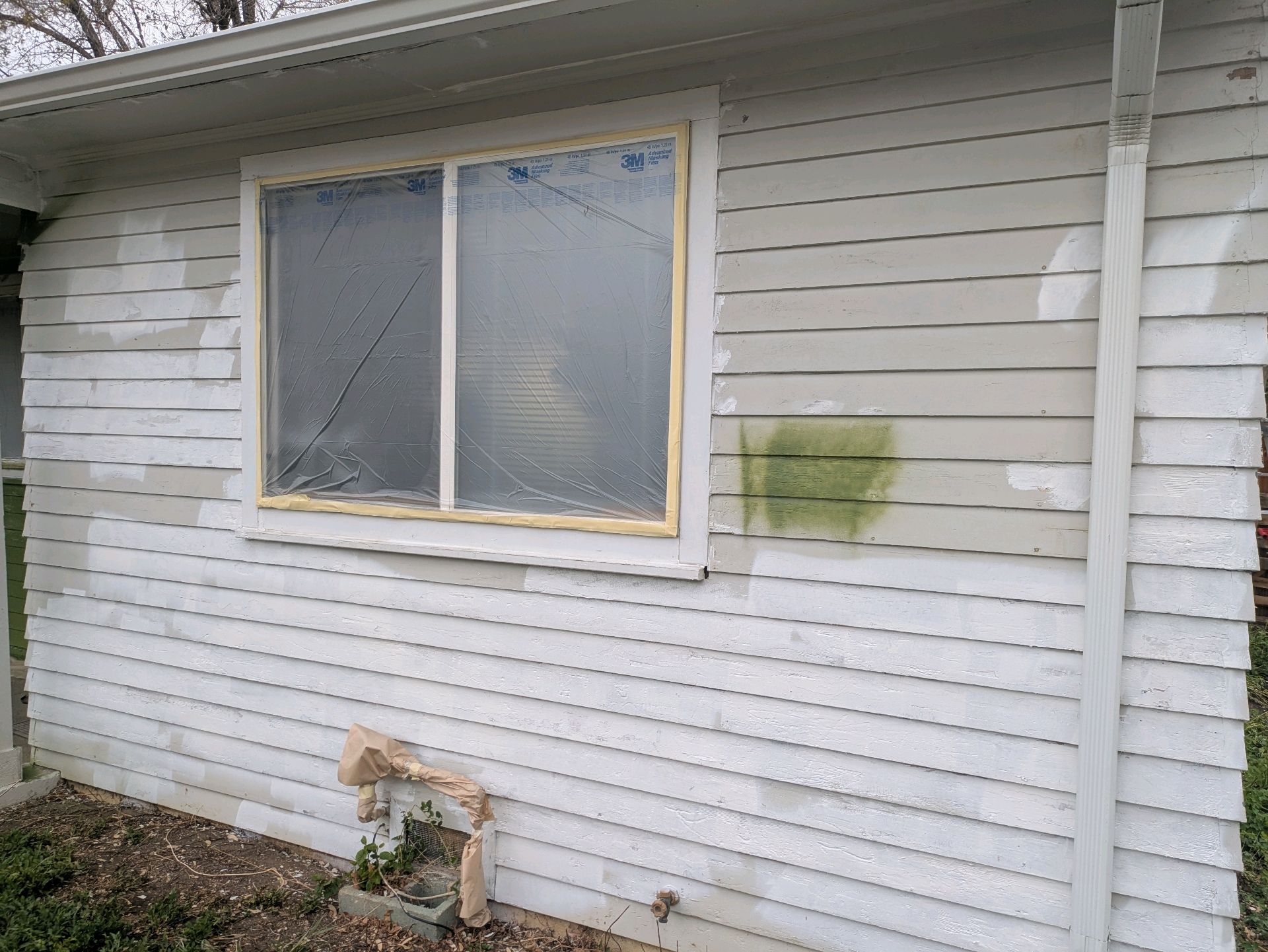 House exterior with white siding, a window, and visible water damage stains near the wall.