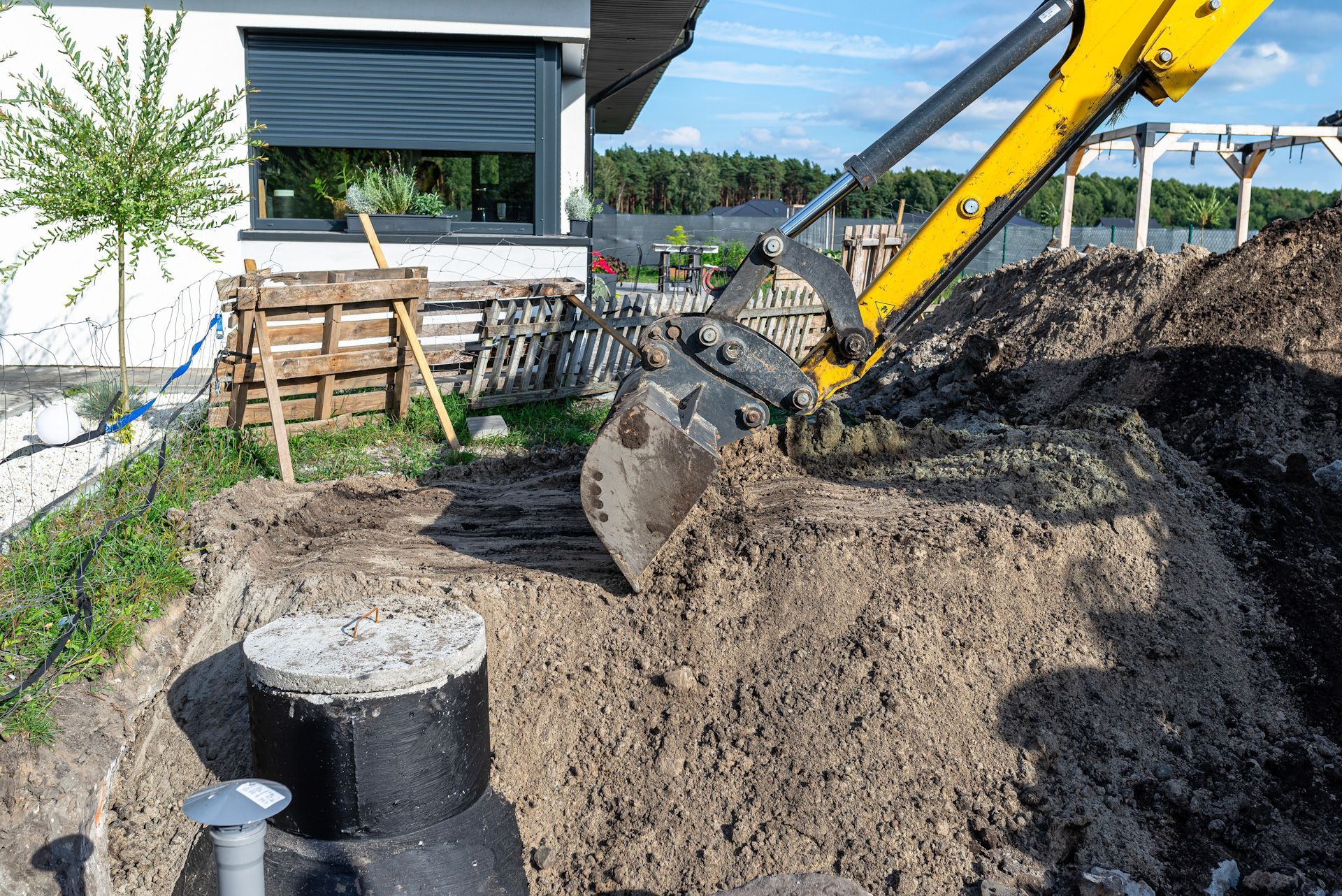 A yellow excavator is digging a hole in the ground in front of a house.