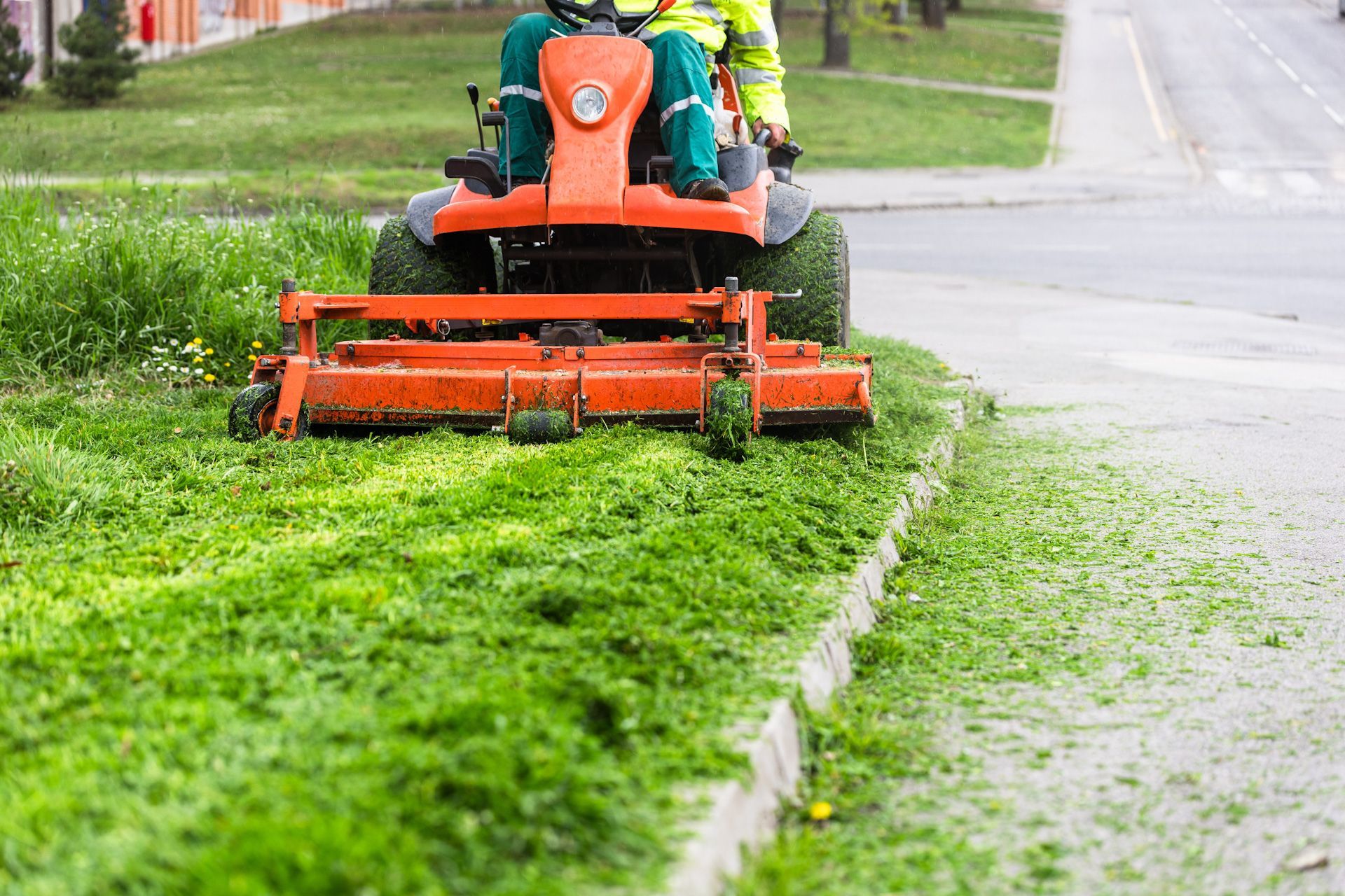 A man is riding a lawn mower on a sidewalk.