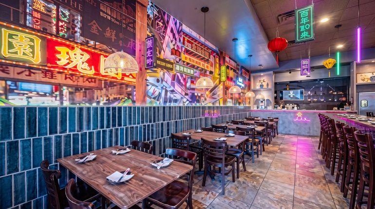 Empty neon-lit Asian restaurant with tiled walls and wooden tables, seen from the dining area.