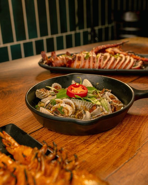 Bowls of plated seafood dishes on a wooden table, topped with herbs and sliced red pepper