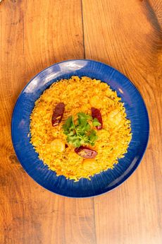 Blue plate with yellow rice, garnished with herbs and chili, on a wooden table