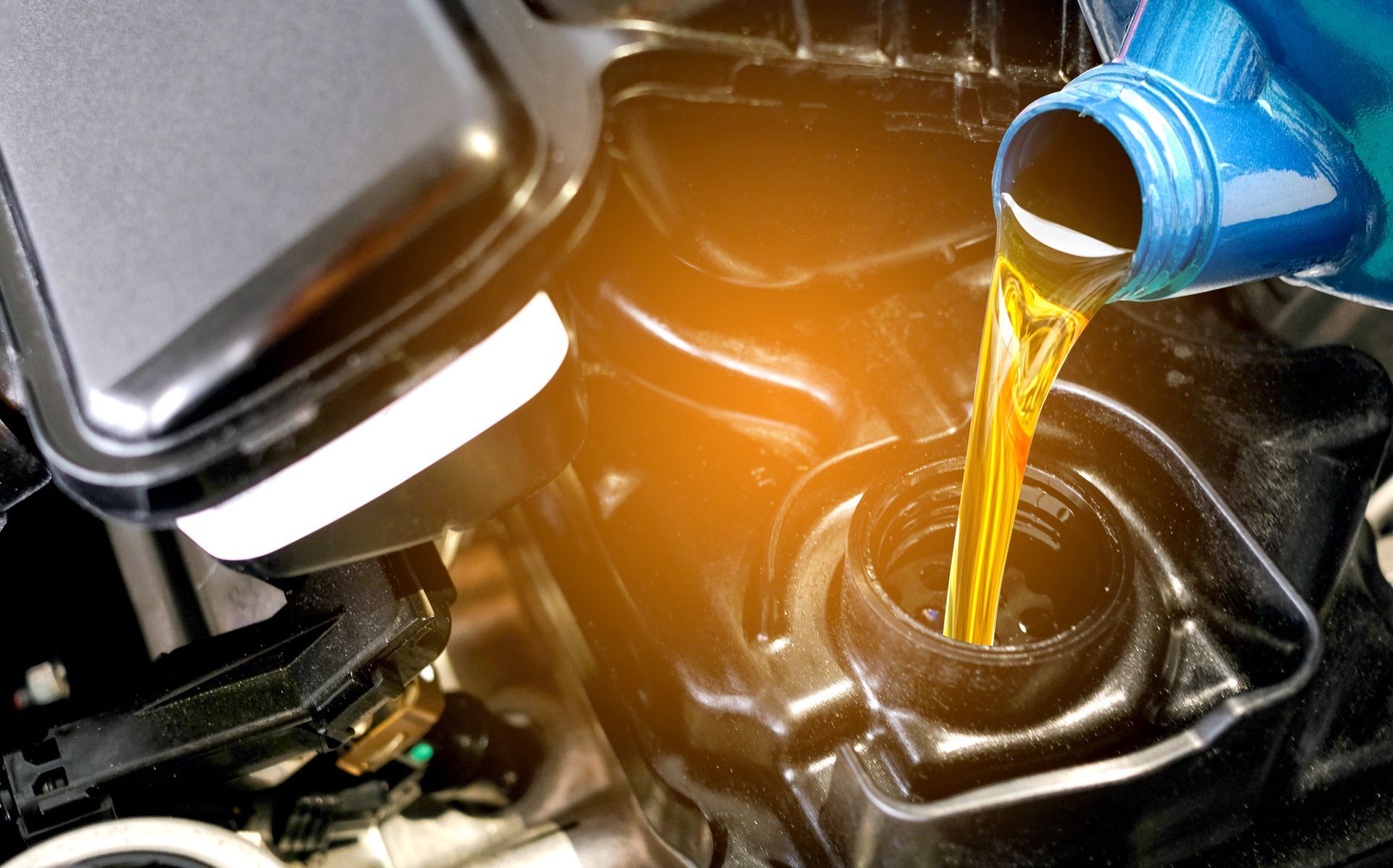 Motor oil being poured from a blue container into a car engine