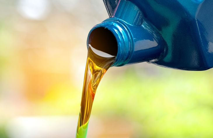 Golden motor oil pouring from a blue bottle spout into a container