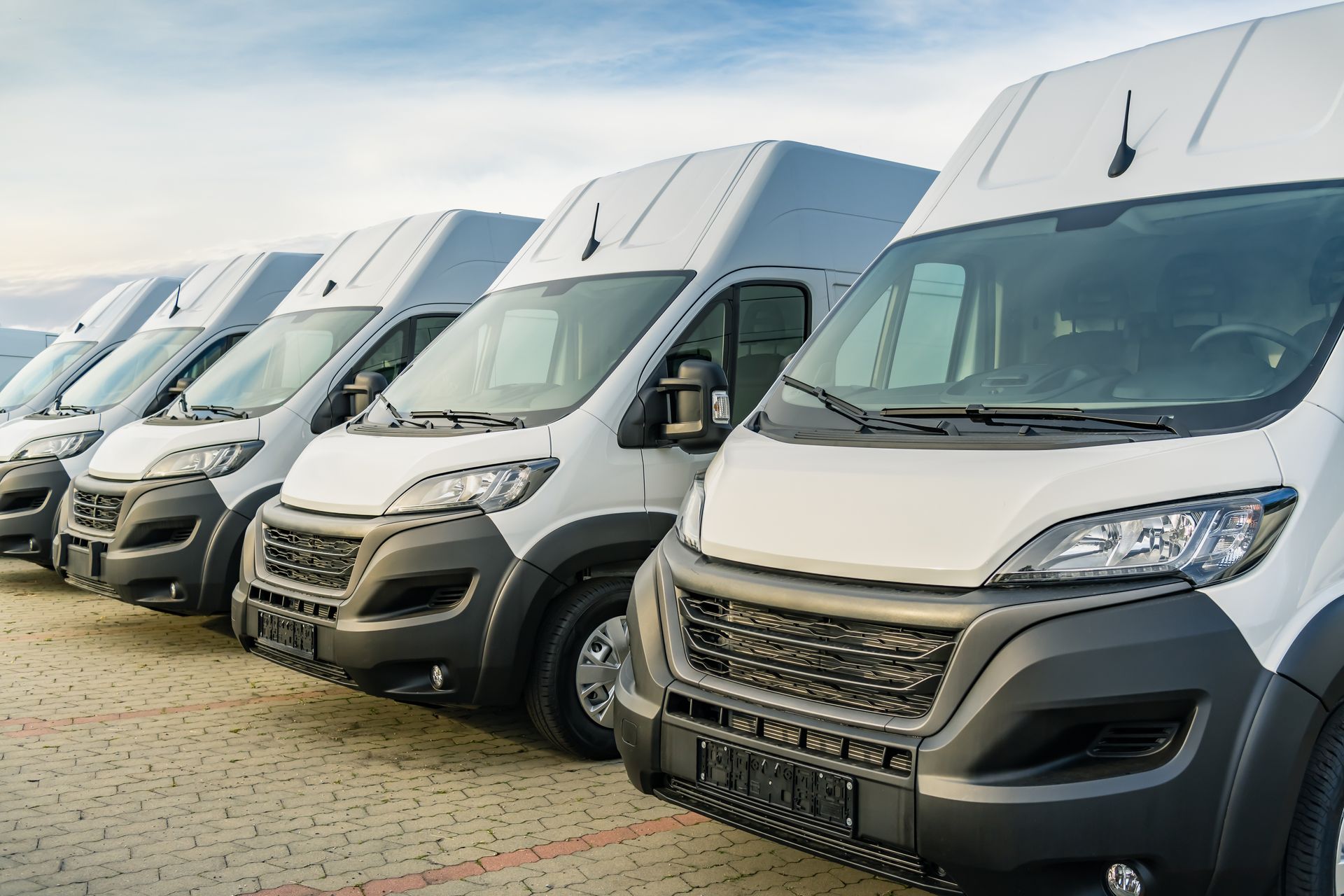 Row of white cargo vans parked outdoors on a paved lot