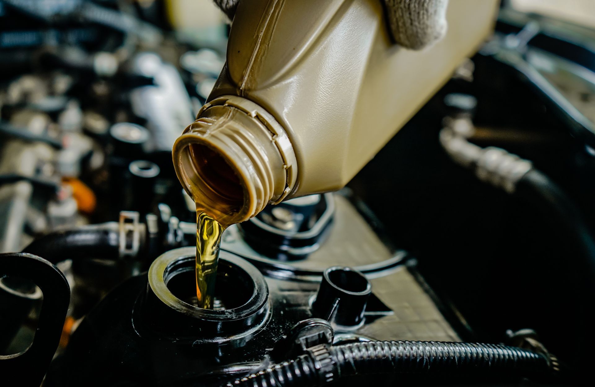 Motor oil being poured from a bottle into a car engine fill cap