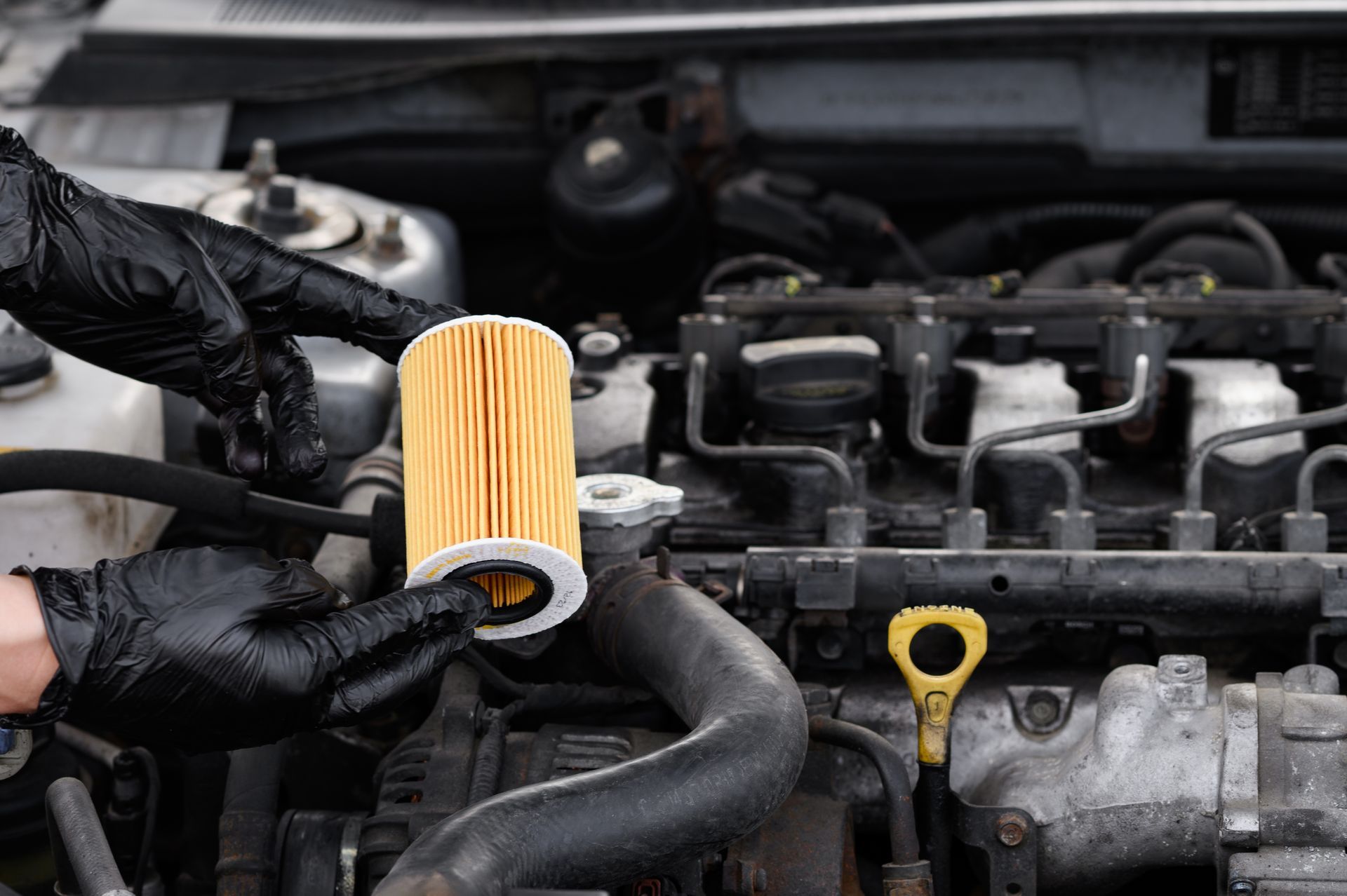 Gloved hands replace a yellow engine air filter under an open car hood.
