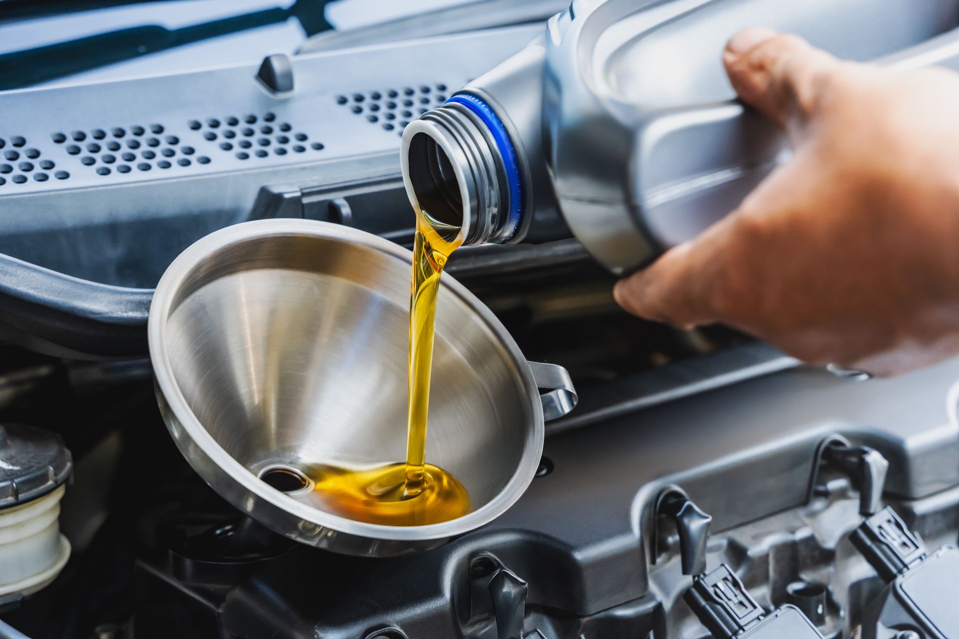 Oil being poured from a bottle into a metal funnel in a car engine bay.
