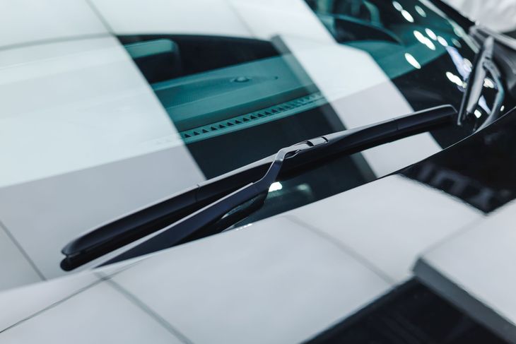 Close-up of a car windshield with wiper blades on a glossy black hood