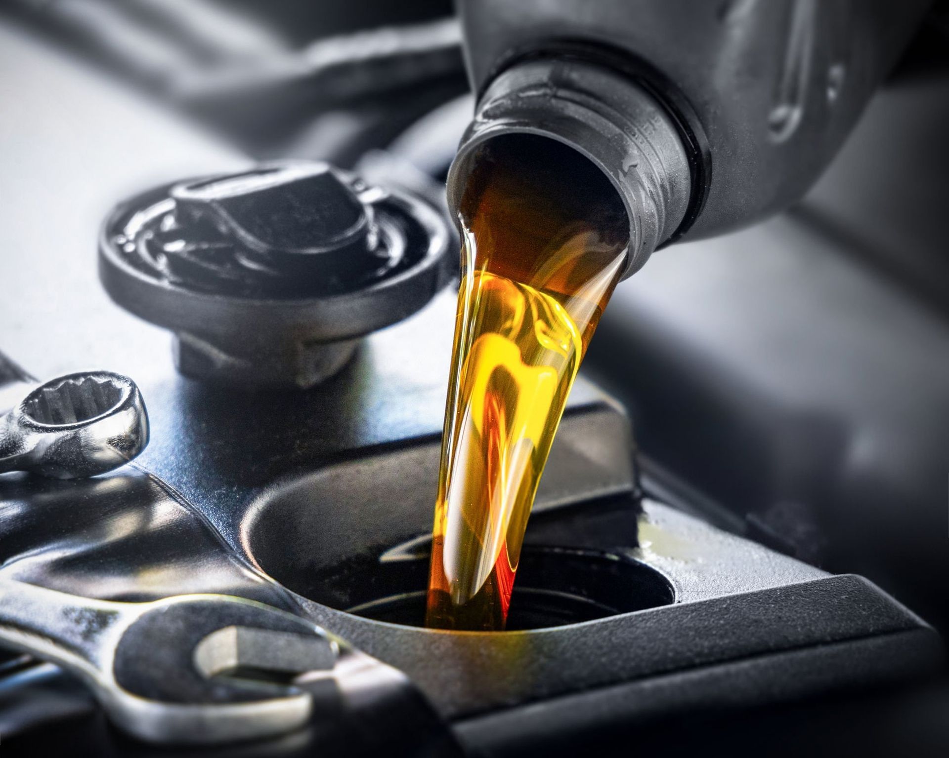 Golden oil pouring from a bottle into a car engine fill port.