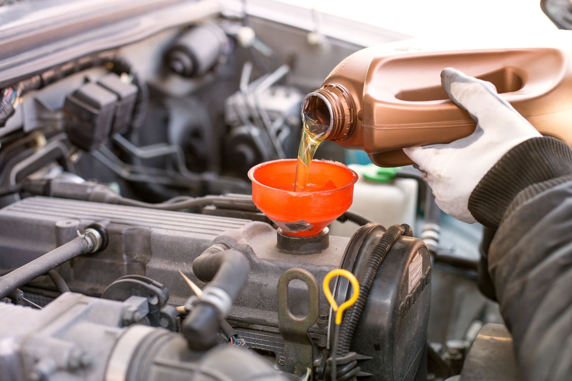 Person pouring orange fluid into a car engine through a funnel