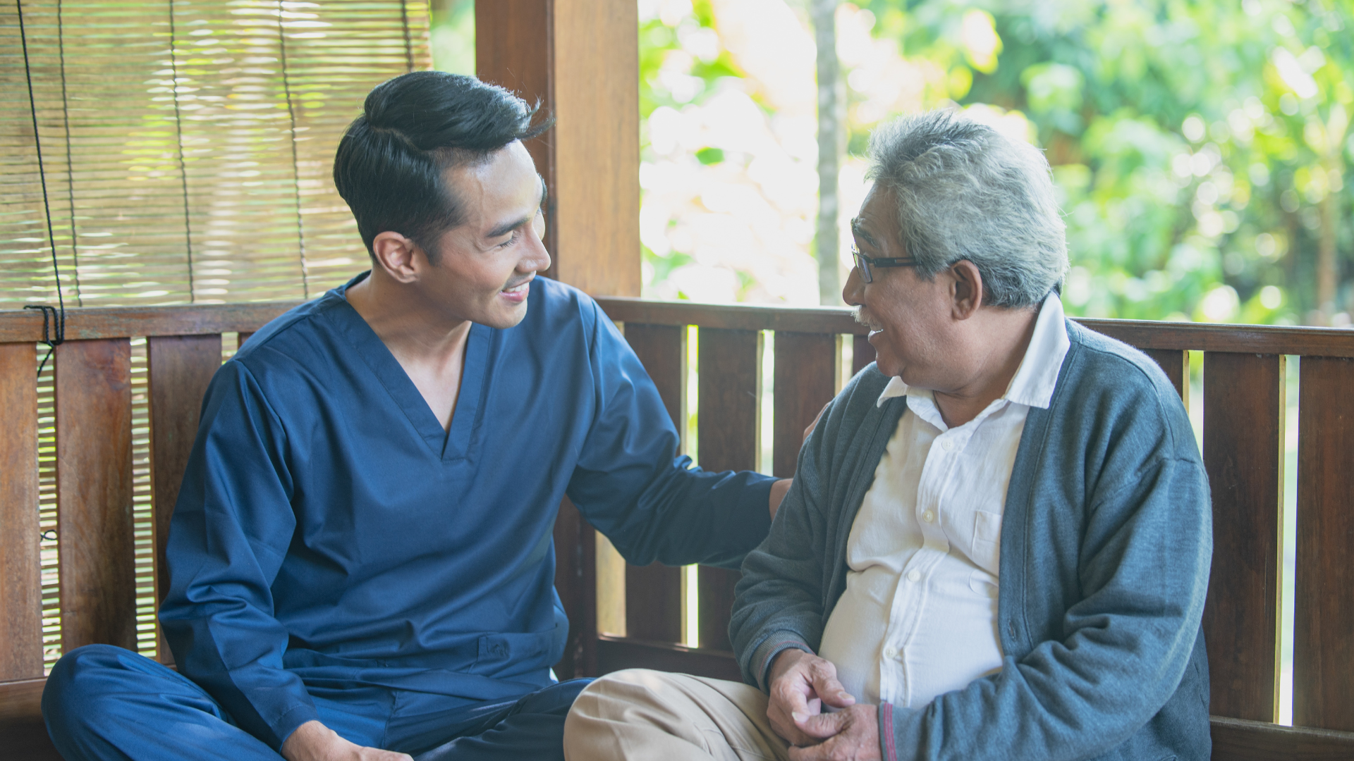 Caregiver holds an elderly person’s hand on a cane, offering support indoors