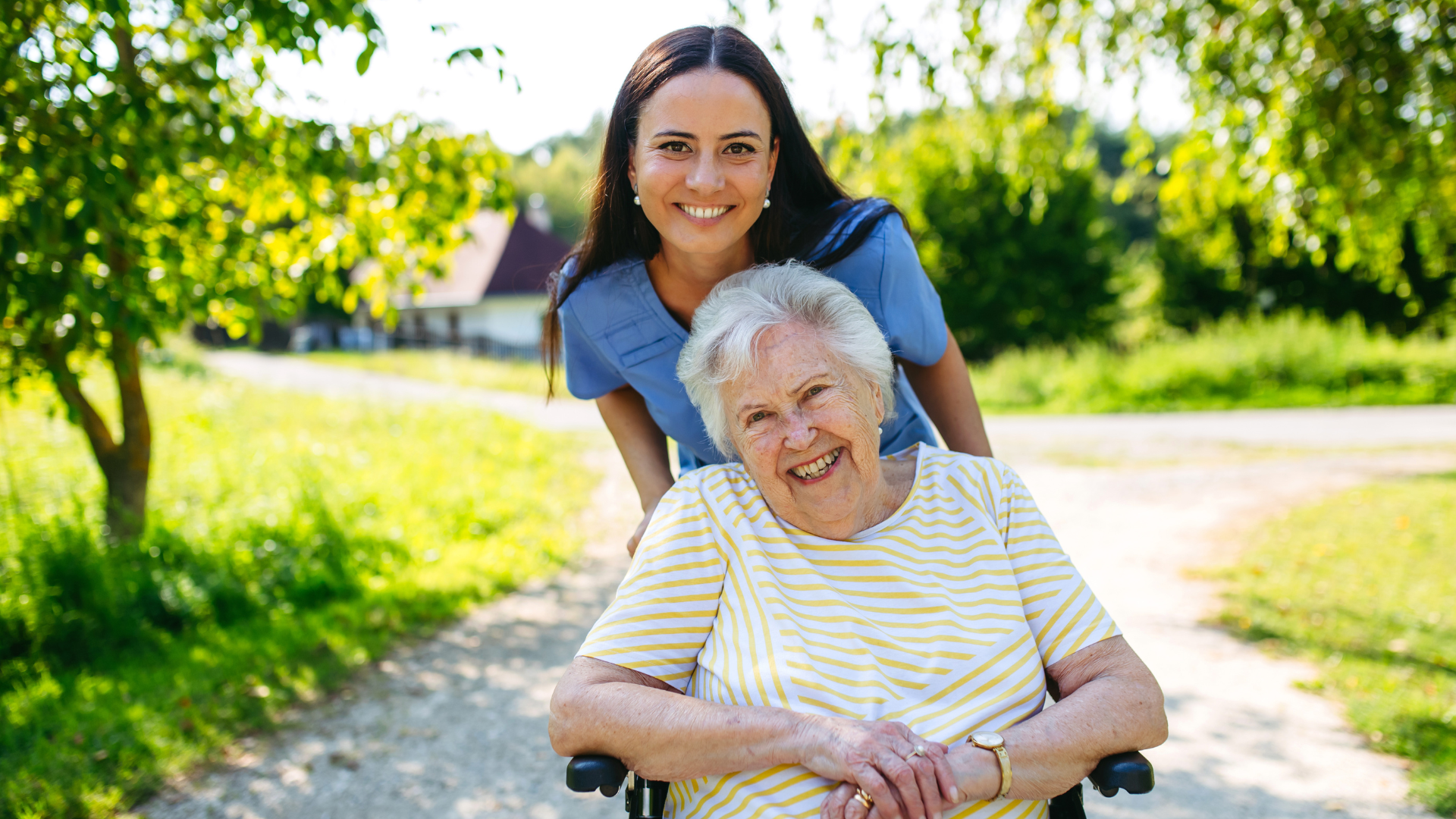 Nurse in blue speaks gently with a smiling patient in a hospital bed