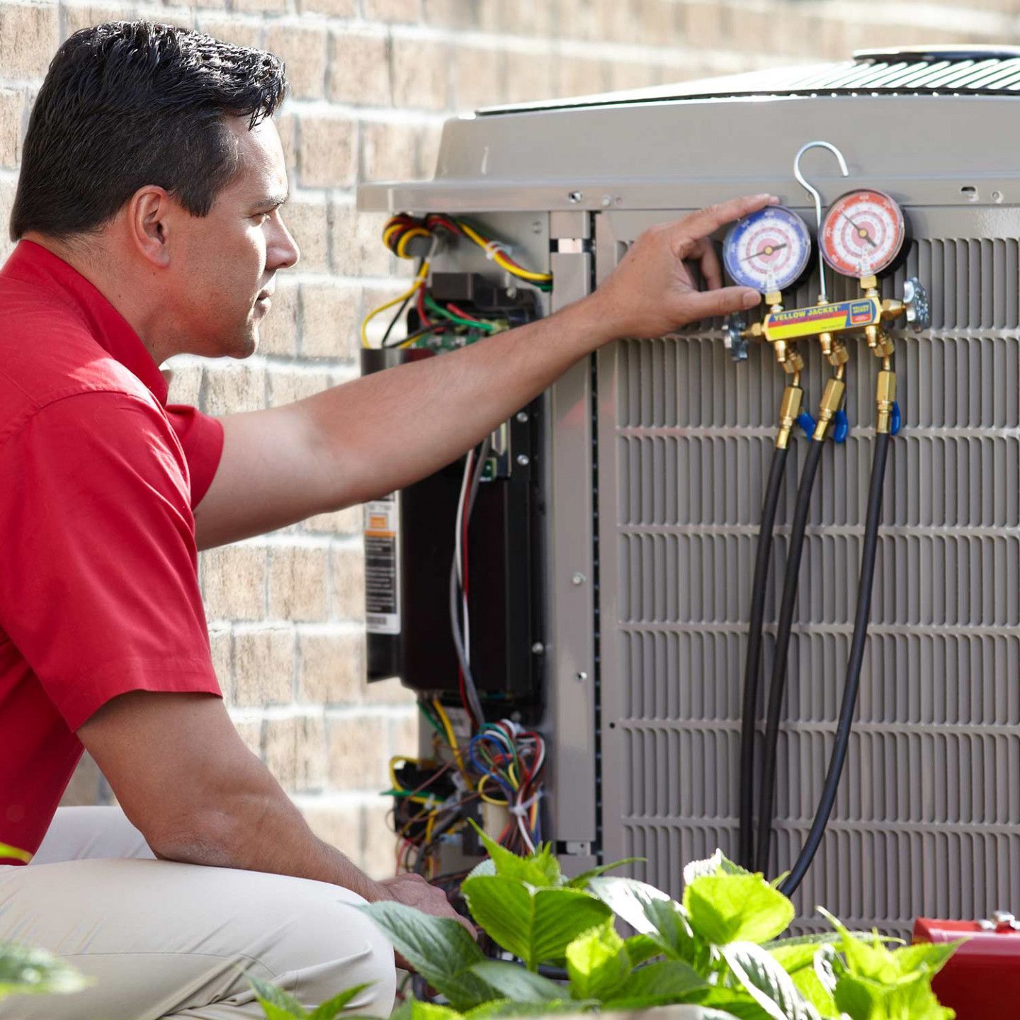 A man in a red shirt is working on an air conditioner