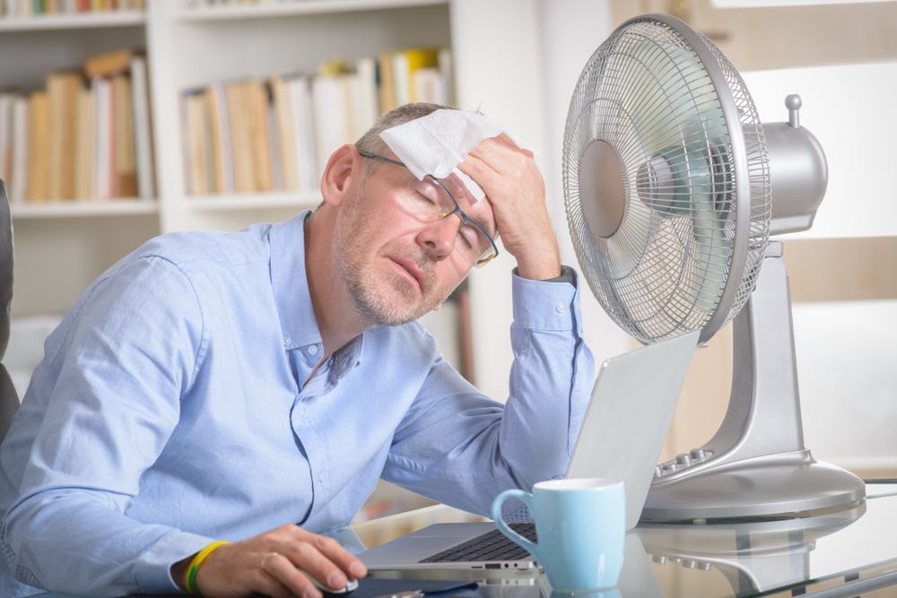A man is sitting at a desk in front of a fan.