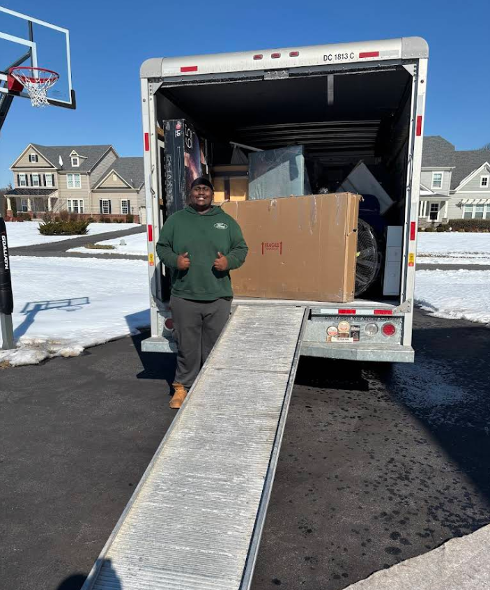 Person beside moving truck unloading a large box down a ramp on a snowy street
